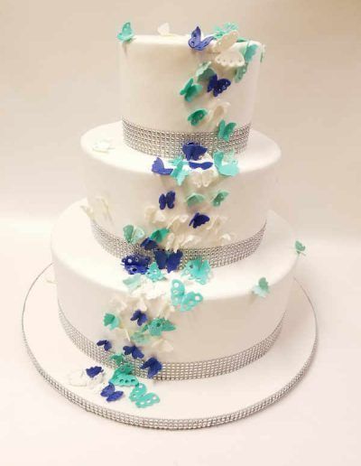 A white wedding cake with blue and green butterflies on it