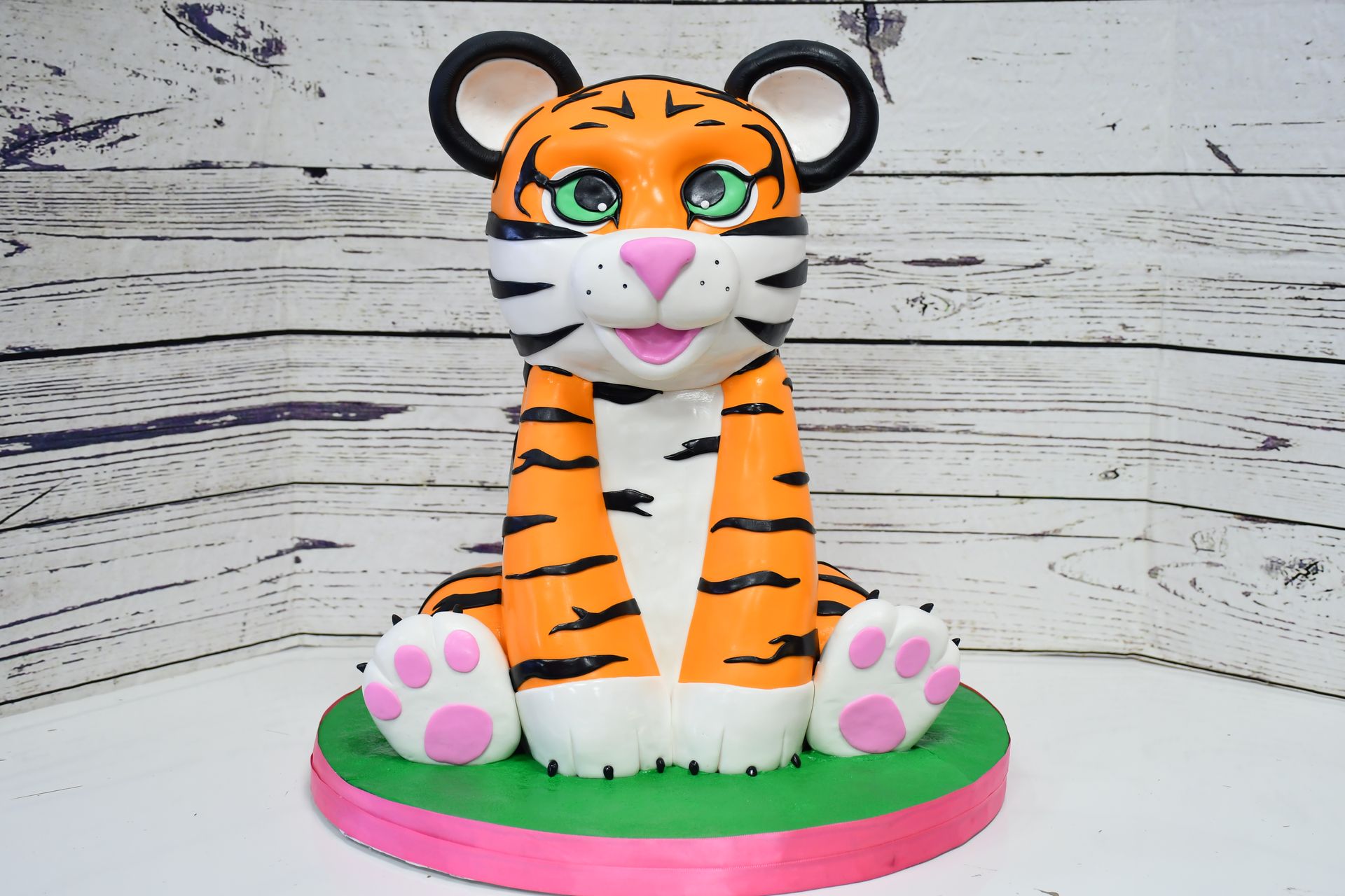 A tiger cake topper is sitting on a pink and green cake stand.
