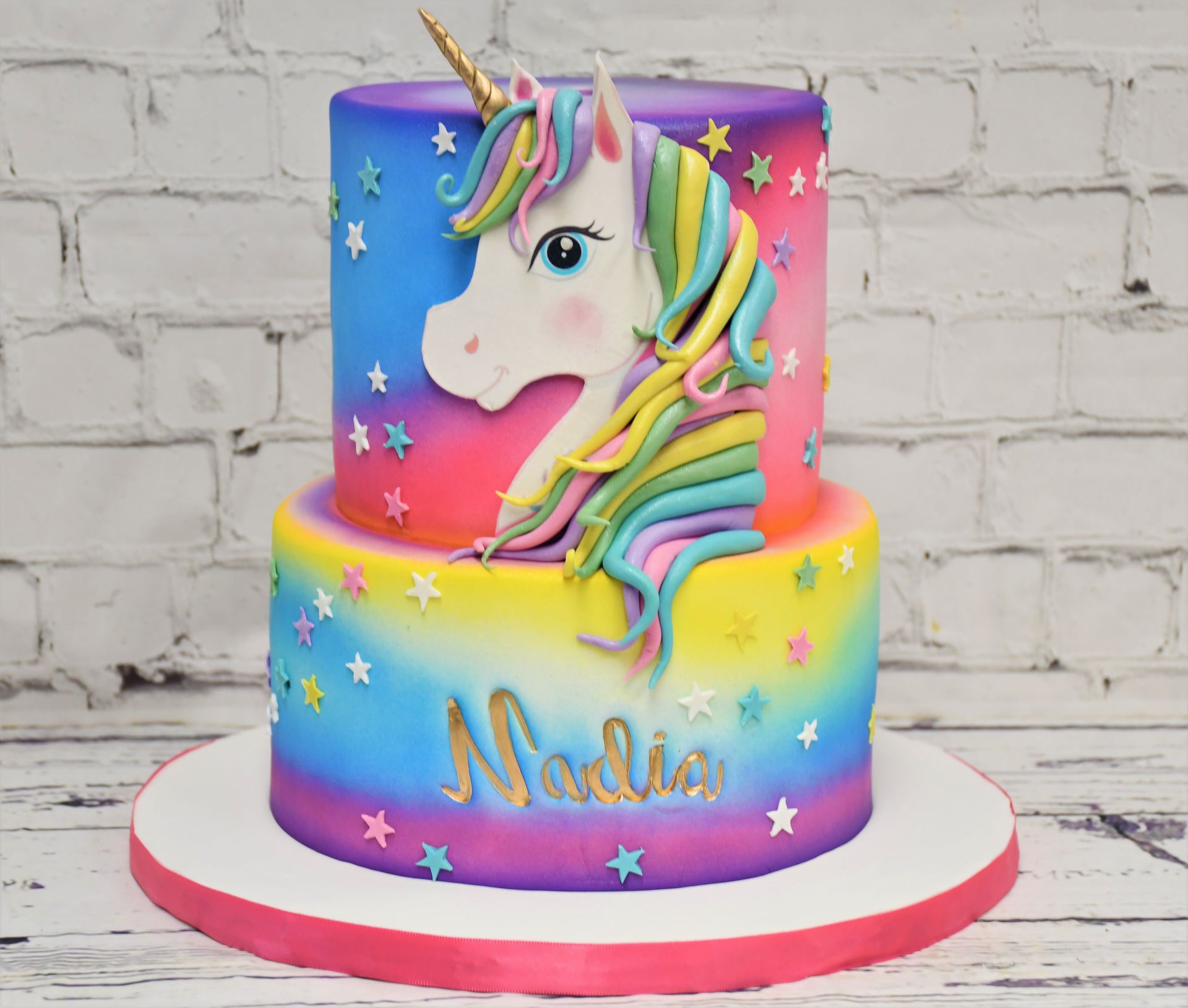A colorful cake with a unicorn and the name nadia on it
