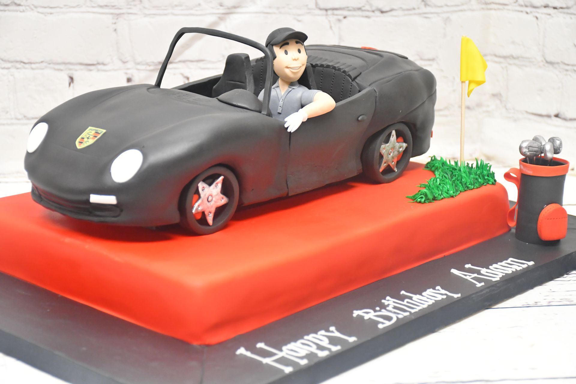 A birthday cake with a black car and a man in it