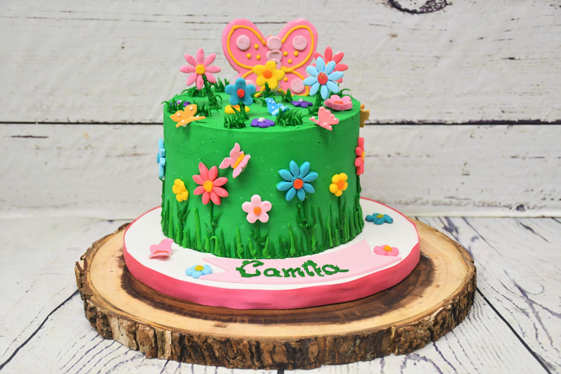 A cake with flowers and butterflies on it is sitting on a wooden stump.