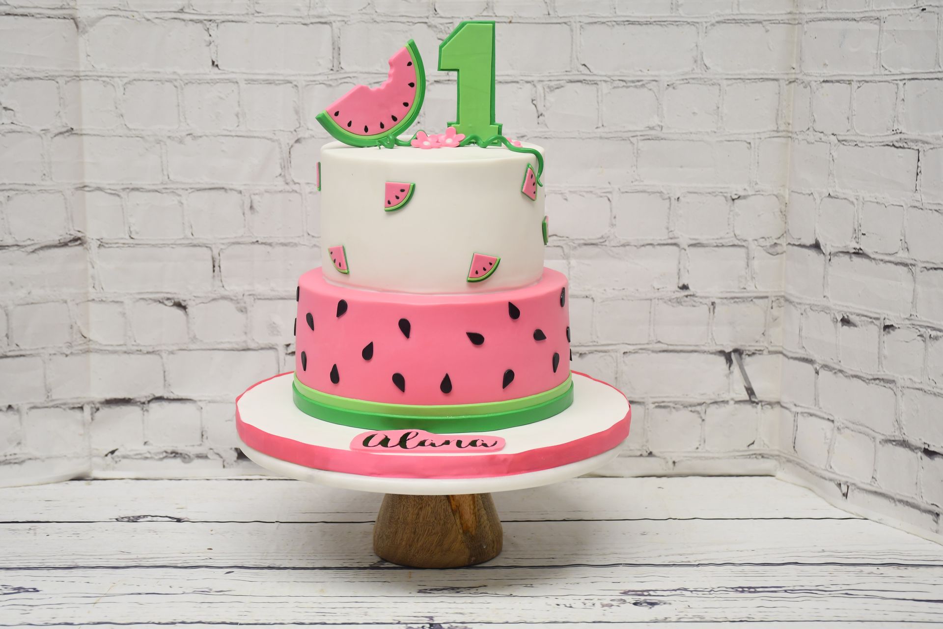 A watermelon cake with a number one on top is on a cake stand.