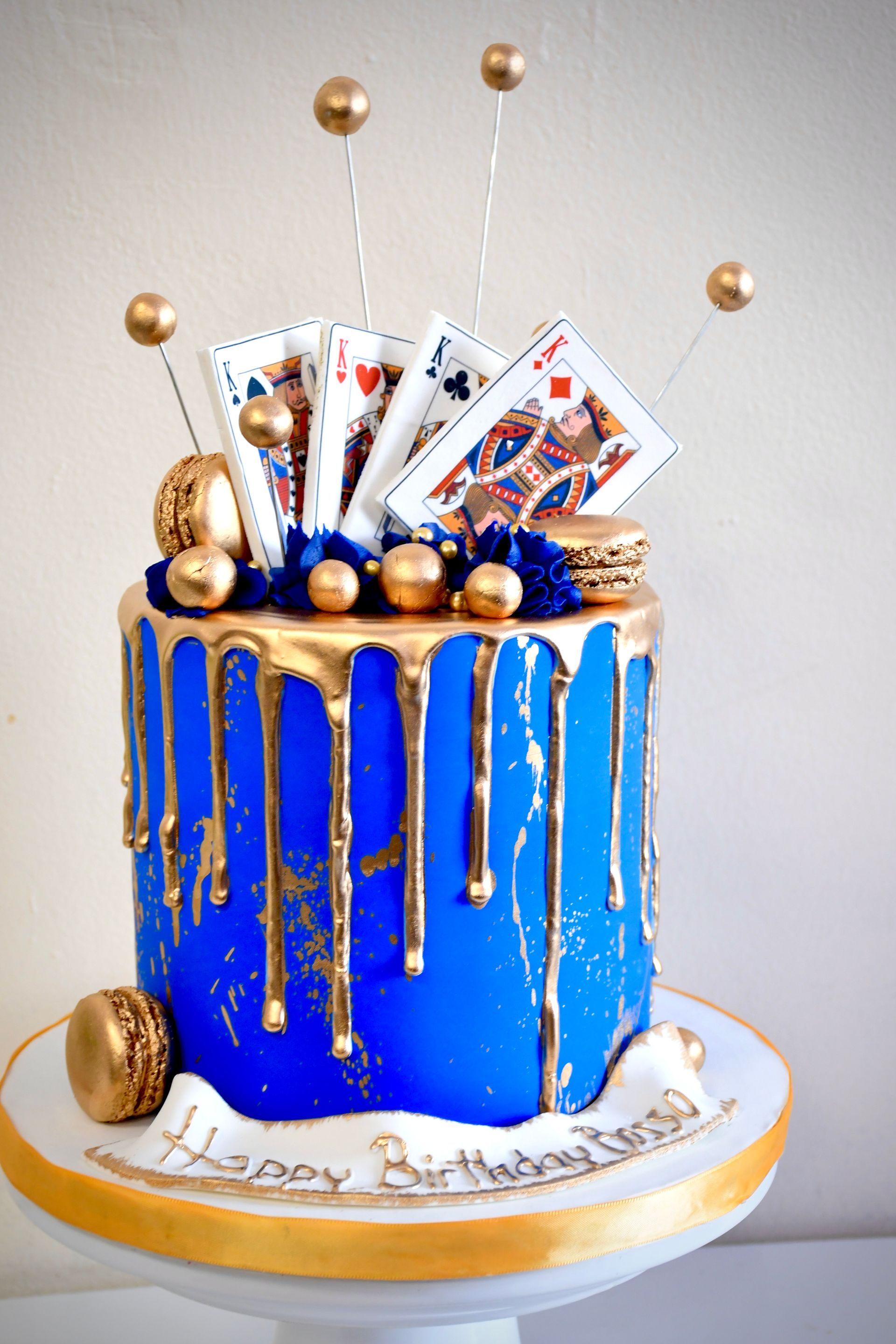 A blue and gold birthday cake with playing cards on top.