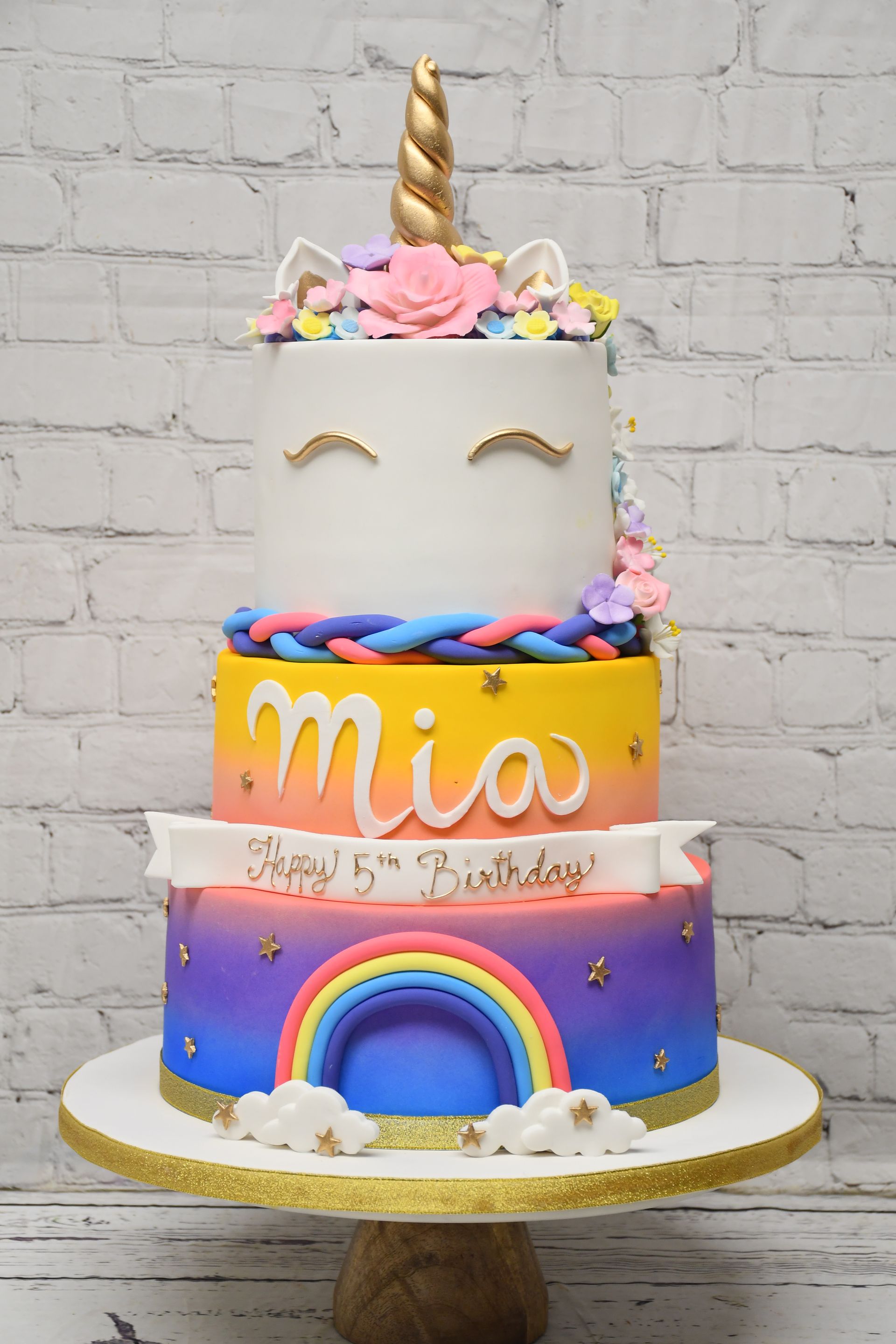 A three tiered unicorn birthday cake with a rainbow on top.
