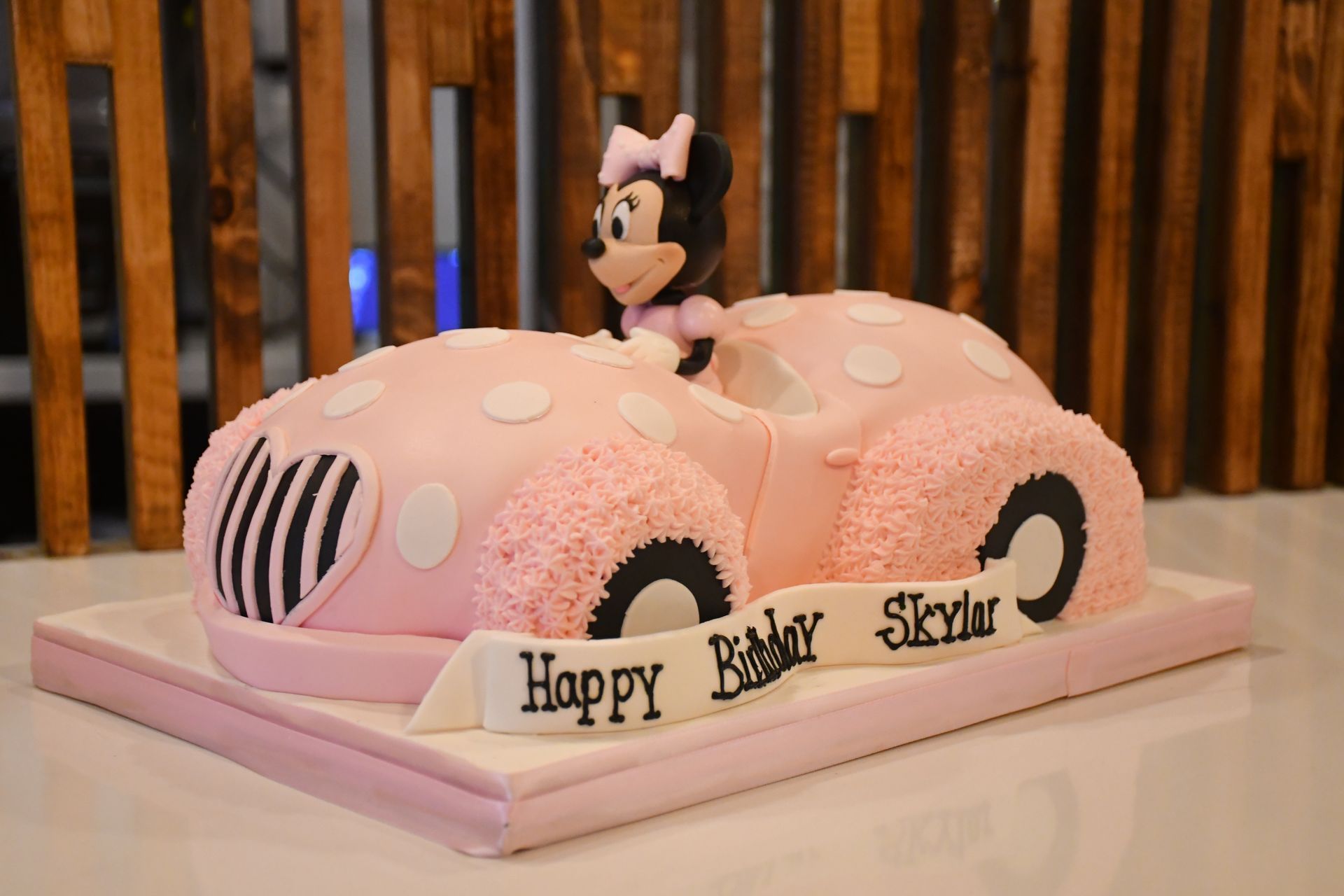 A cake in the shape of a pink car with minnie mouse on top.