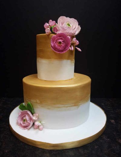 A gold and white cake with pink flowers on top.