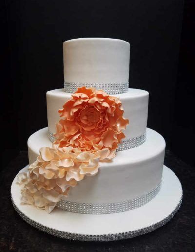 A white wedding cake with an orange flower on top