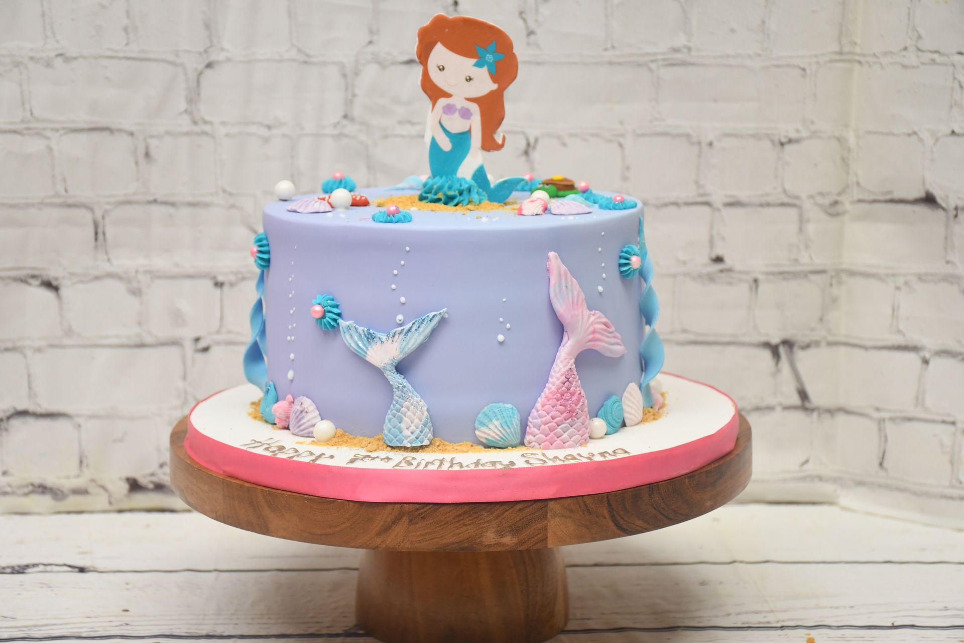 A mermaid cake is sitting on top of a wooden cake stand.