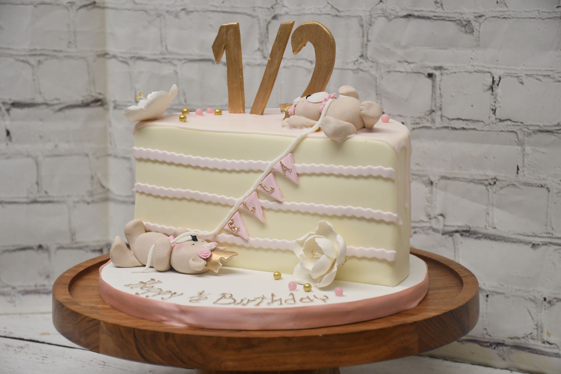A baby 's half birthday cake is sitting on a wooden cake stand.