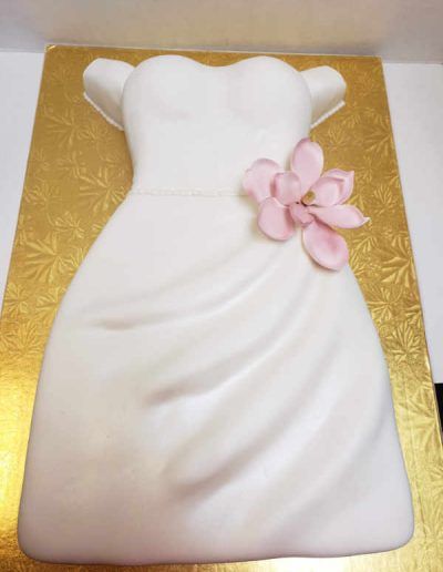 A white cake in the shape of a wedding dress with a pink flower on it.