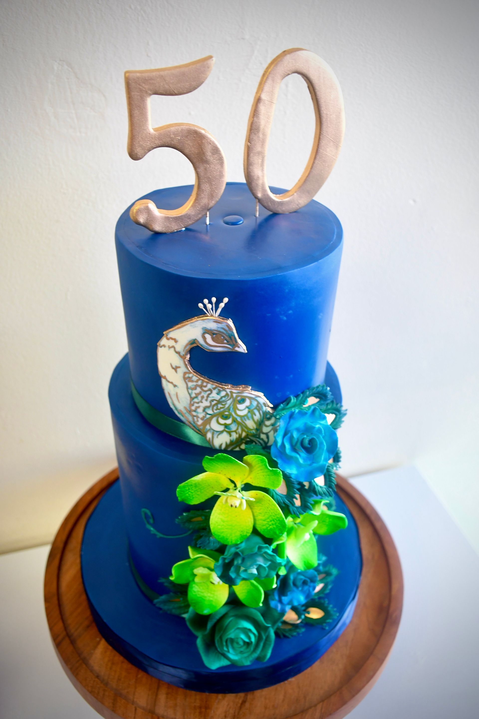 A blue cake with a peacock and the number 50 on top