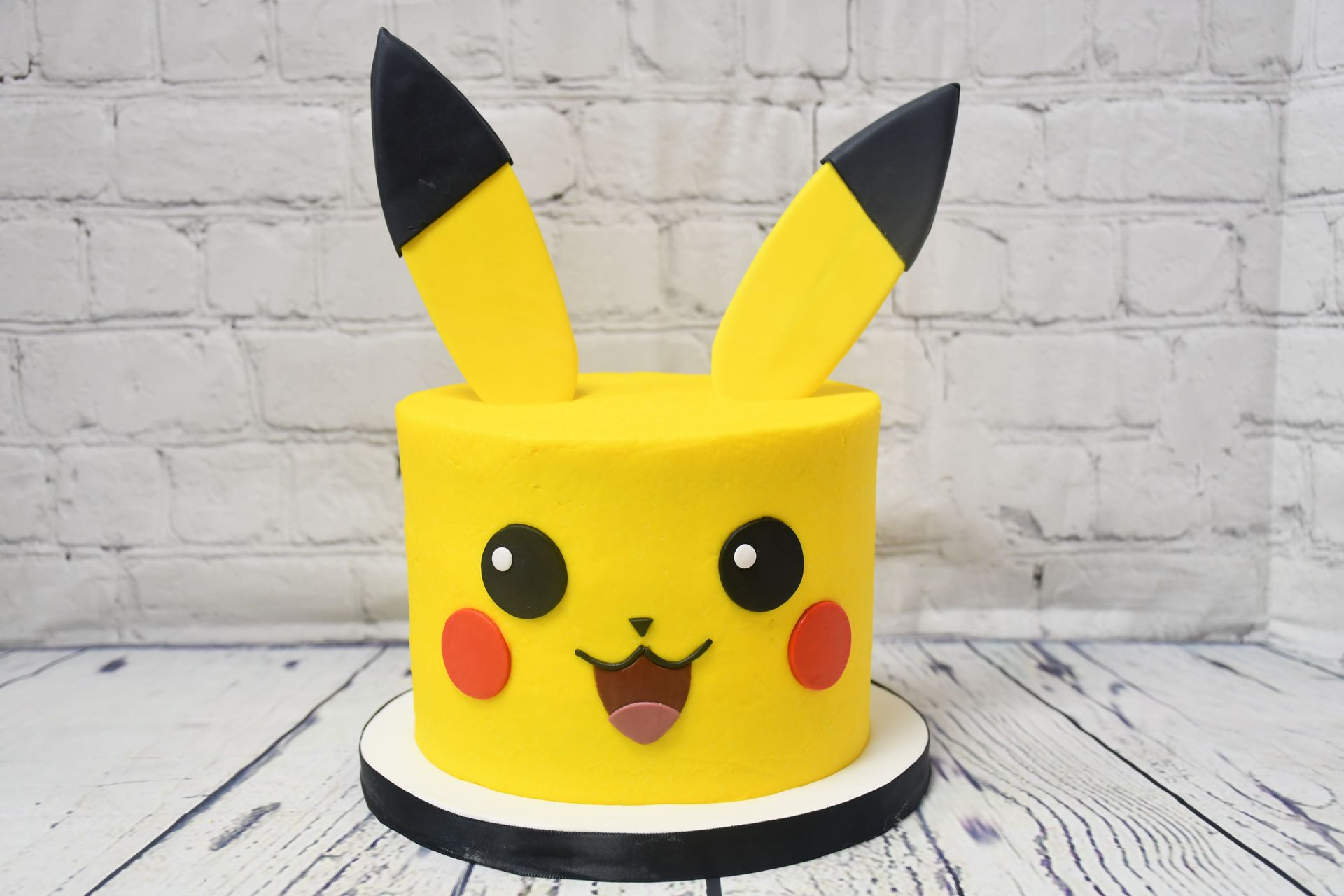 A yellow cake with a pikachu face on it is sitting on a wooden table.
