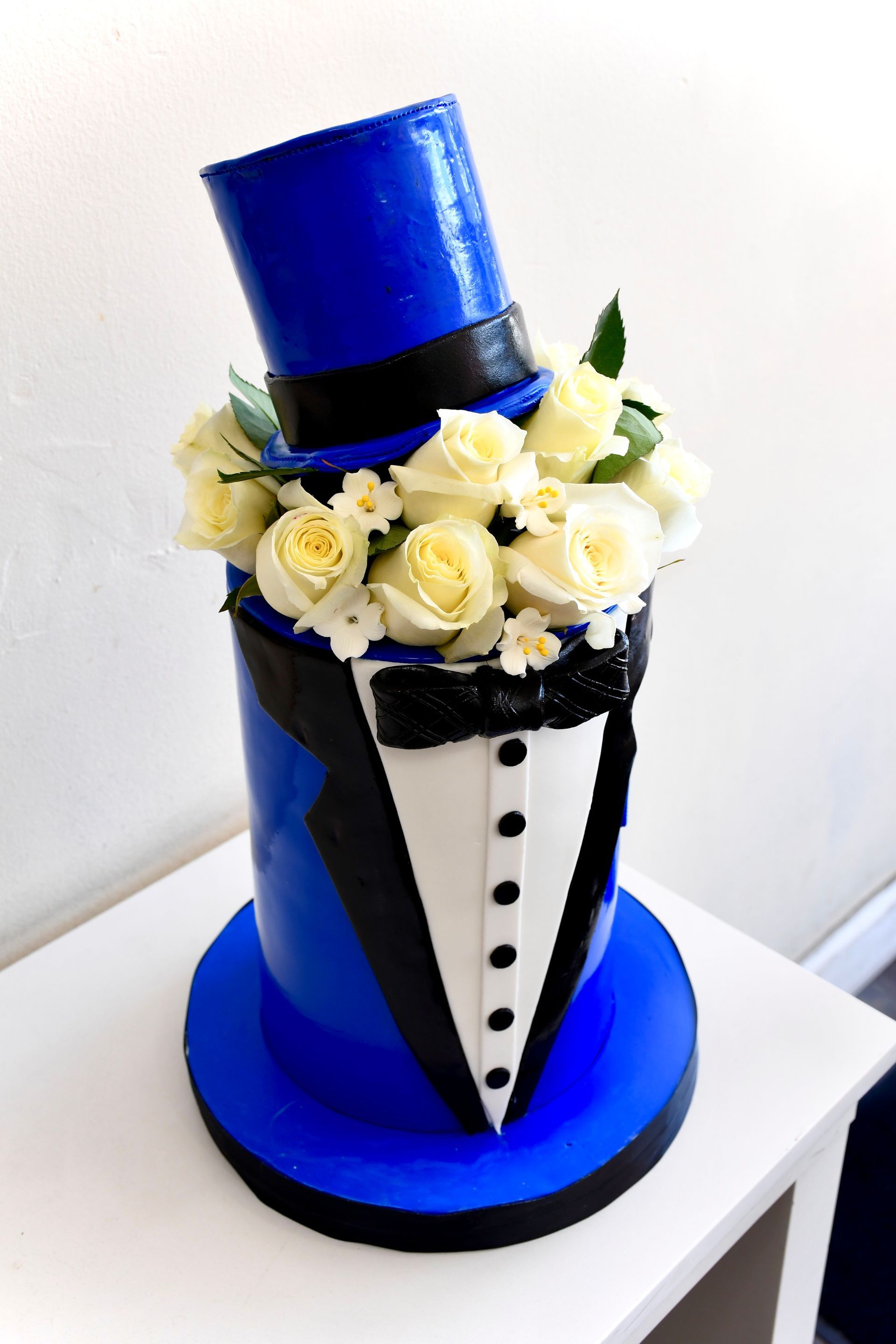 A blue top hat and tuxedo cake with white roses