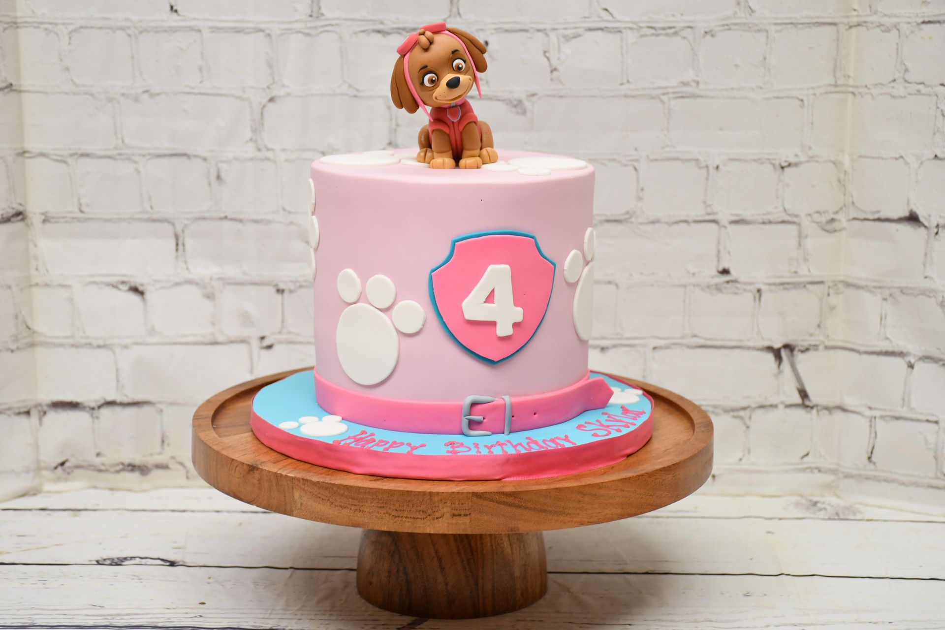 A pink paw patrol cake with a dog on top is on a wooden cake stand.