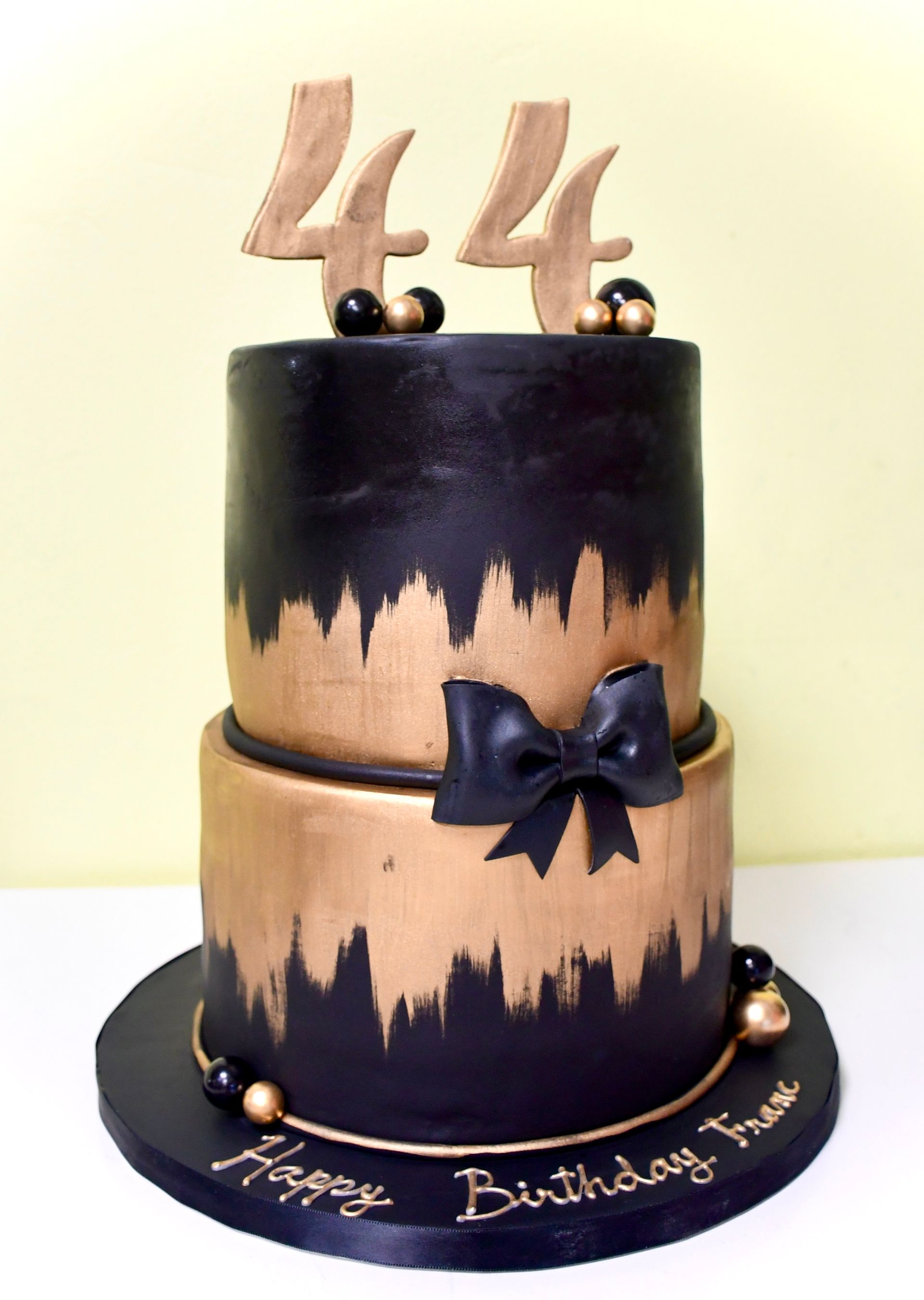 A black and gold birthday cake with the number 44 on top.