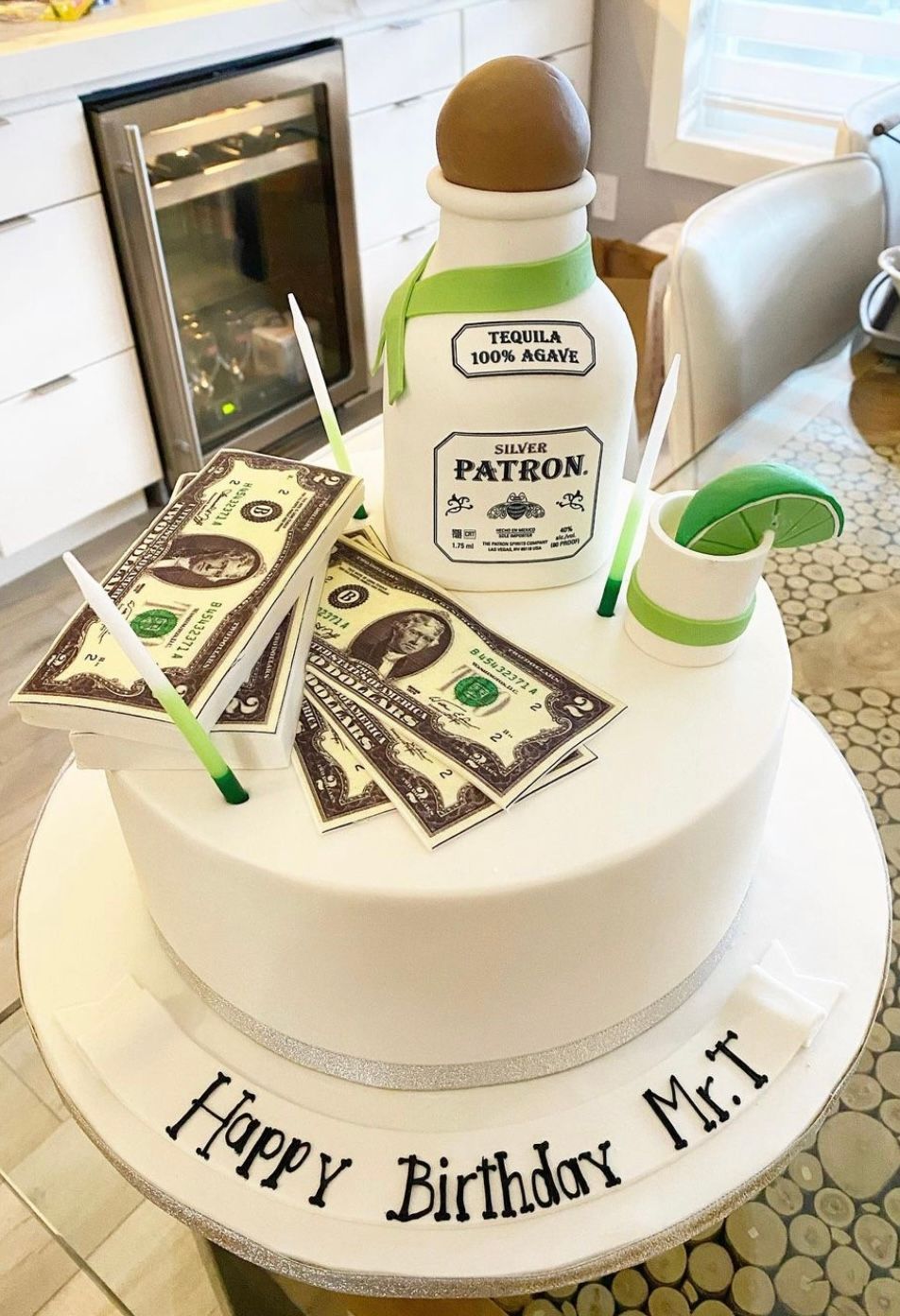 A birthday cake with a bottle of patron tequila and money on it.