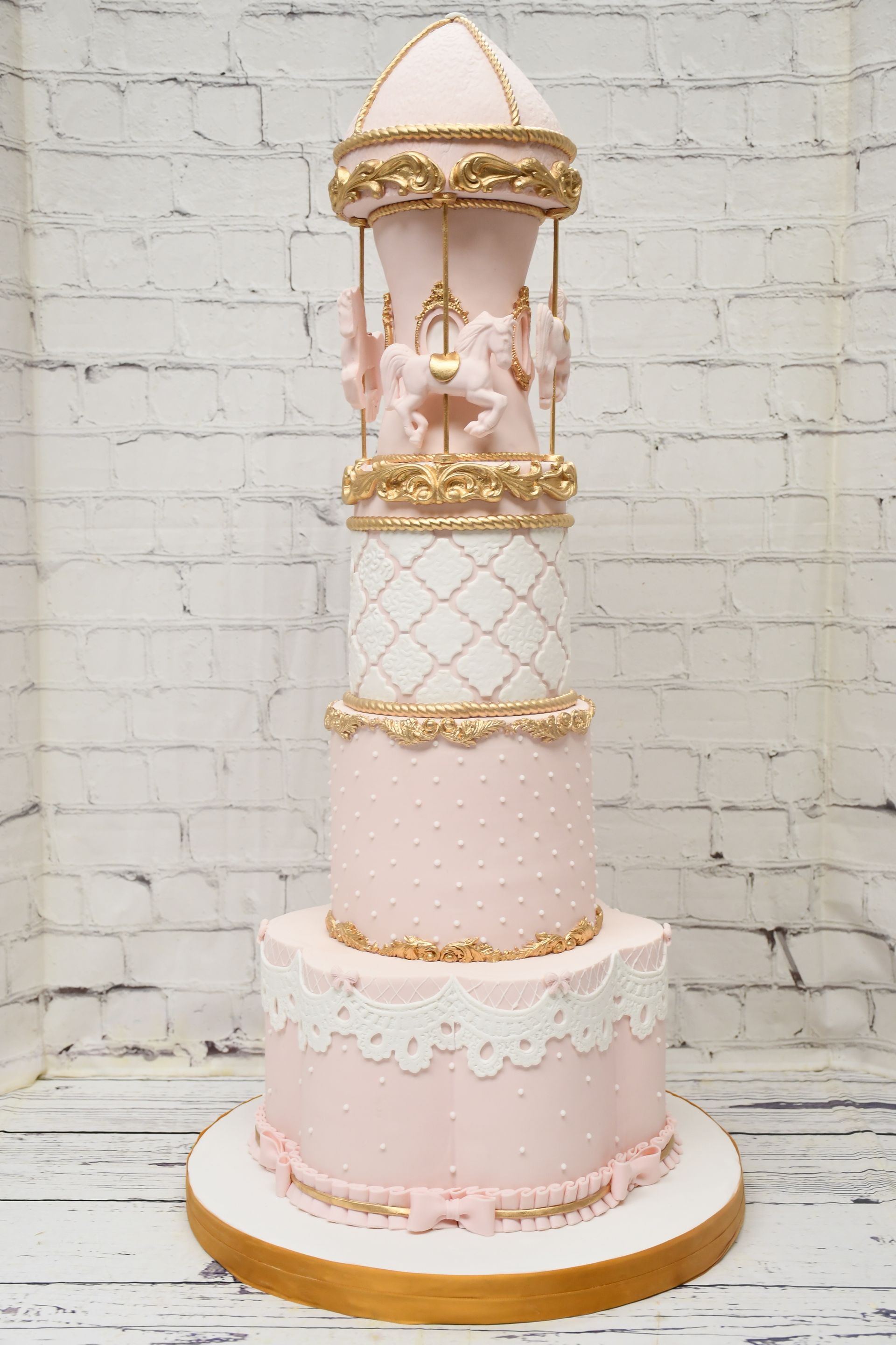A pink and white cake with a merry go round on top of it.
