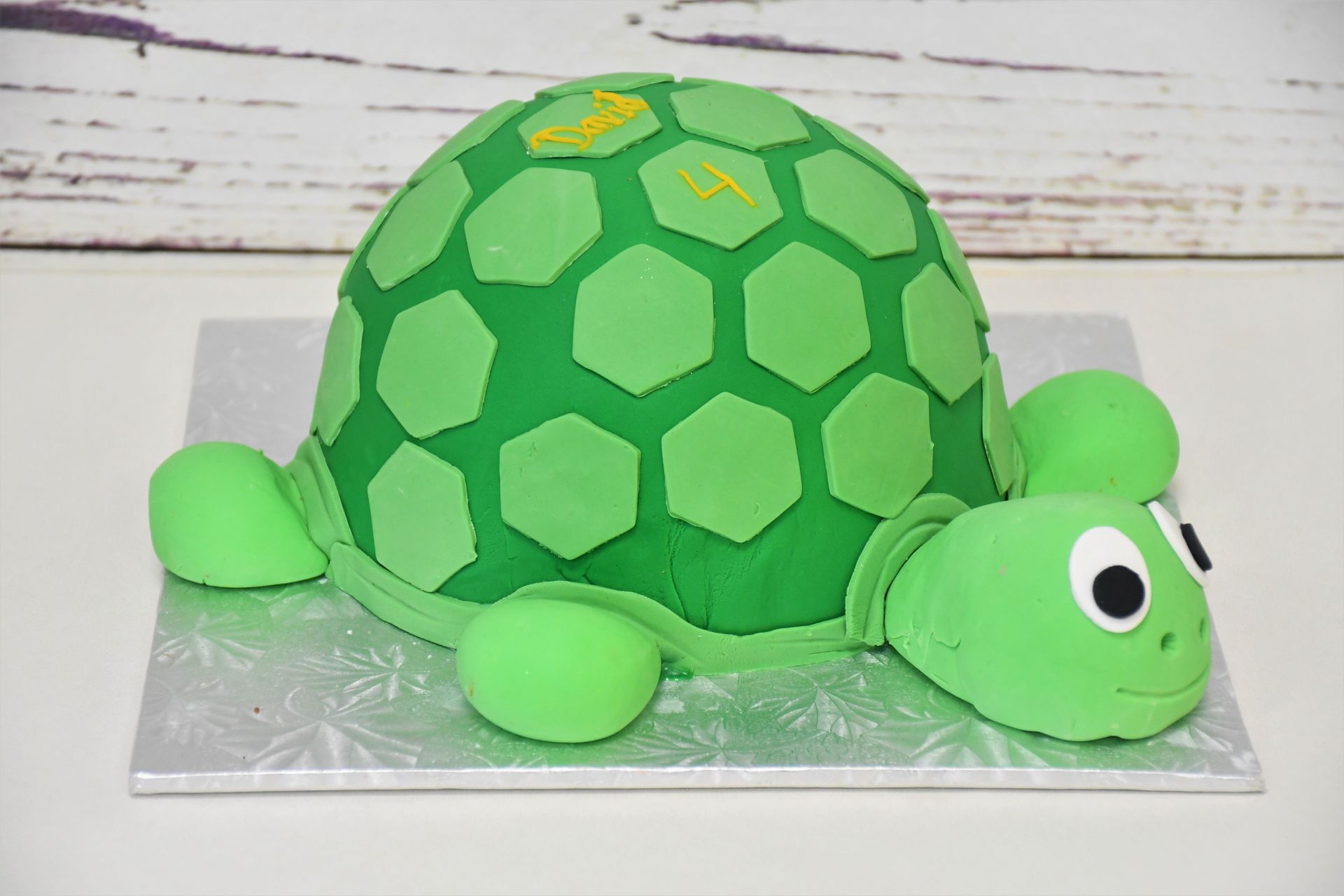 A green turtle cake is sitting on a silver plate on a table.