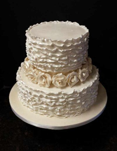 A white cake with ruffles and roses on it