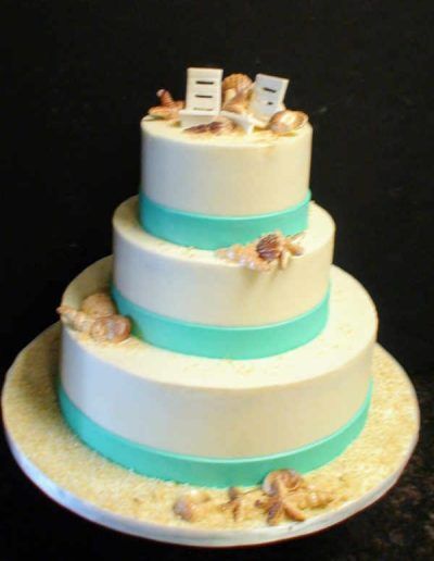 A white cake with blue ribbons and seashells on top