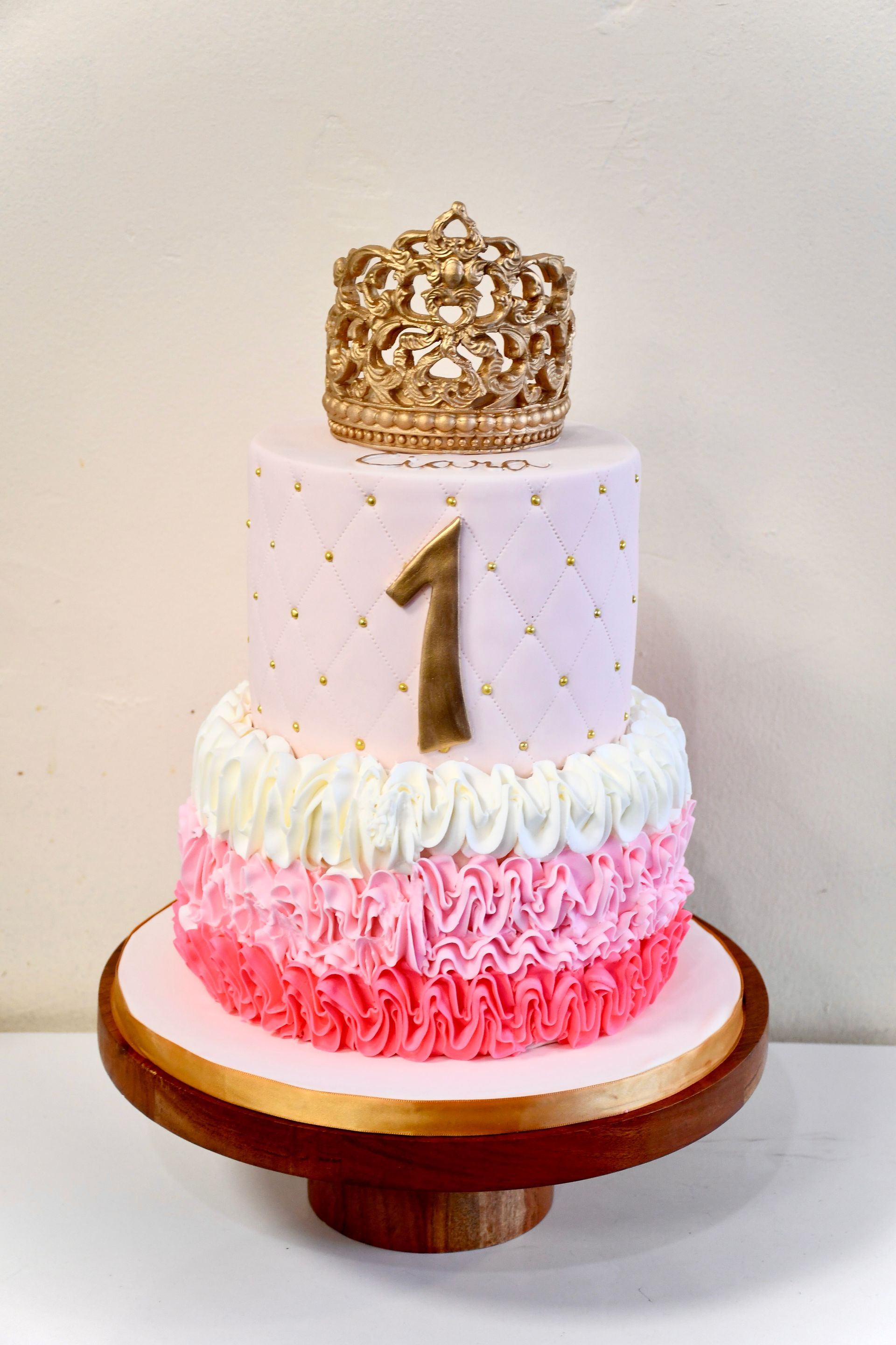 A pink and white birthday cake with a gold crown on top.