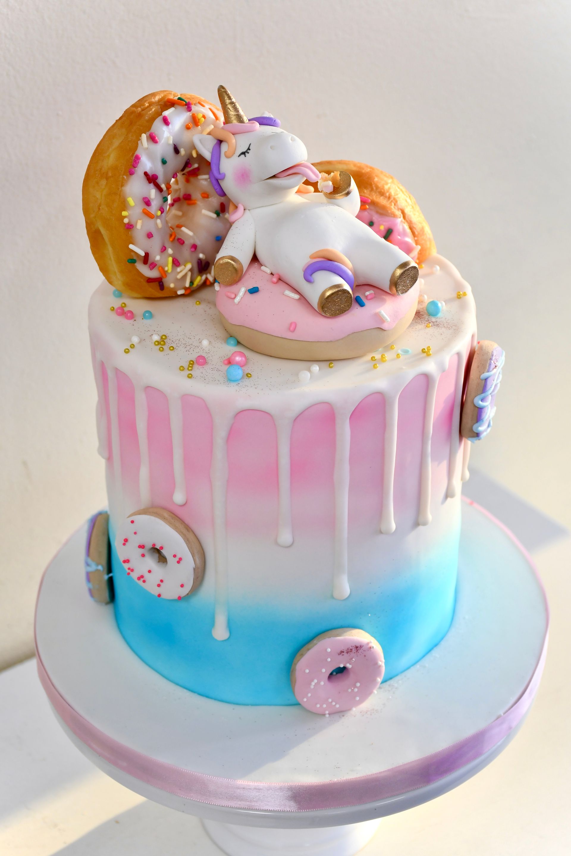 A cake with a unicorn and donuts on top of it.