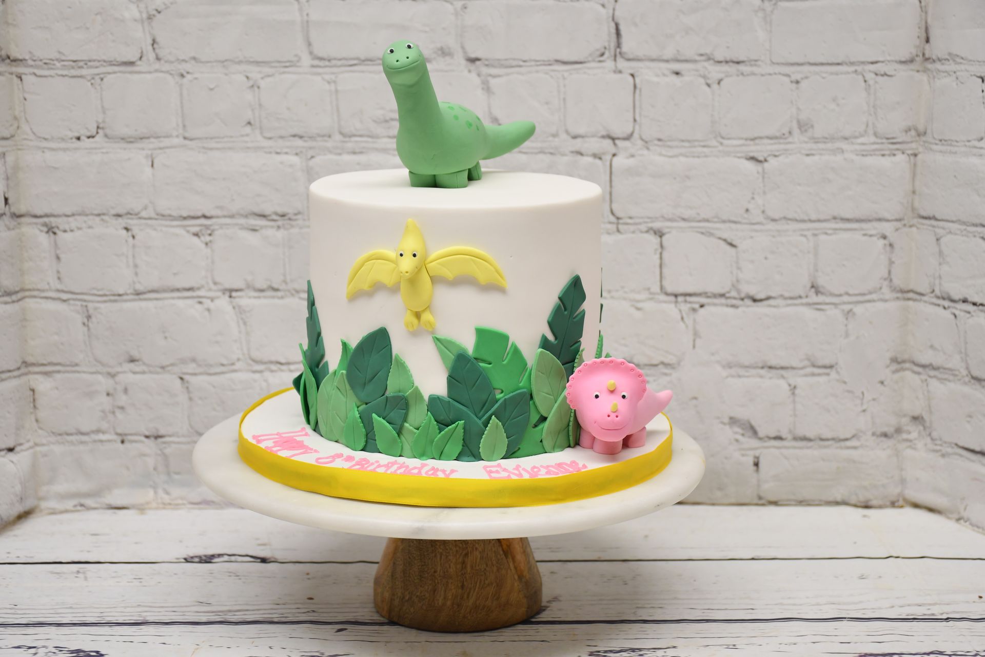 A cake with a dinosaur on top of it is on a cake stand.