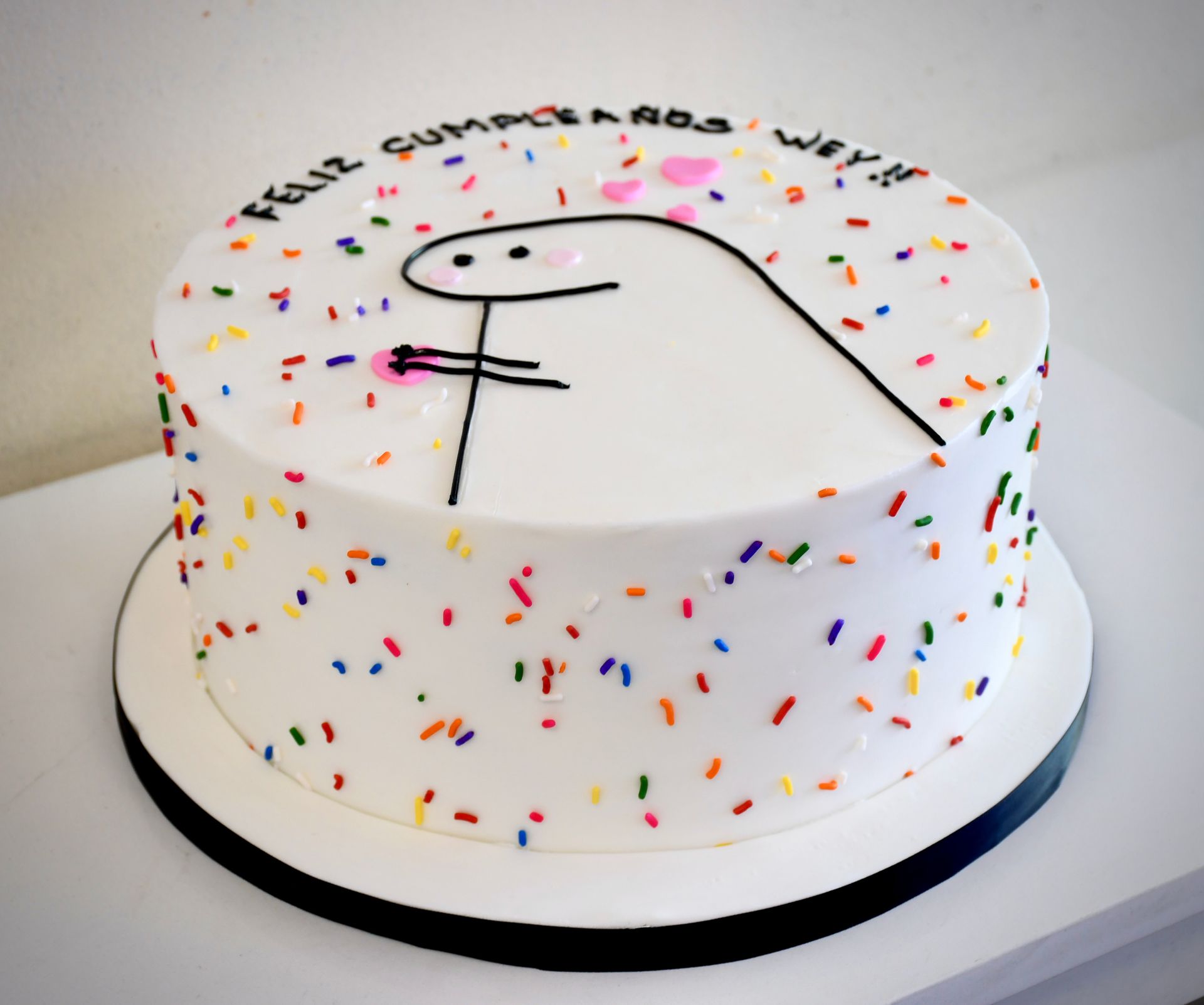 A white cake with sprinkles and the words feliz cumpleanos written on it