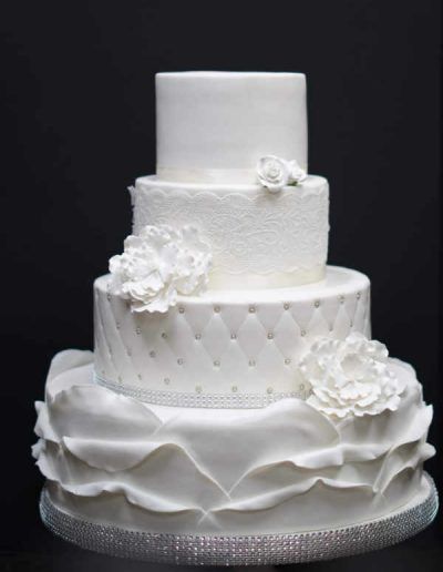 A white wedding cake with ruffles and flowers on it