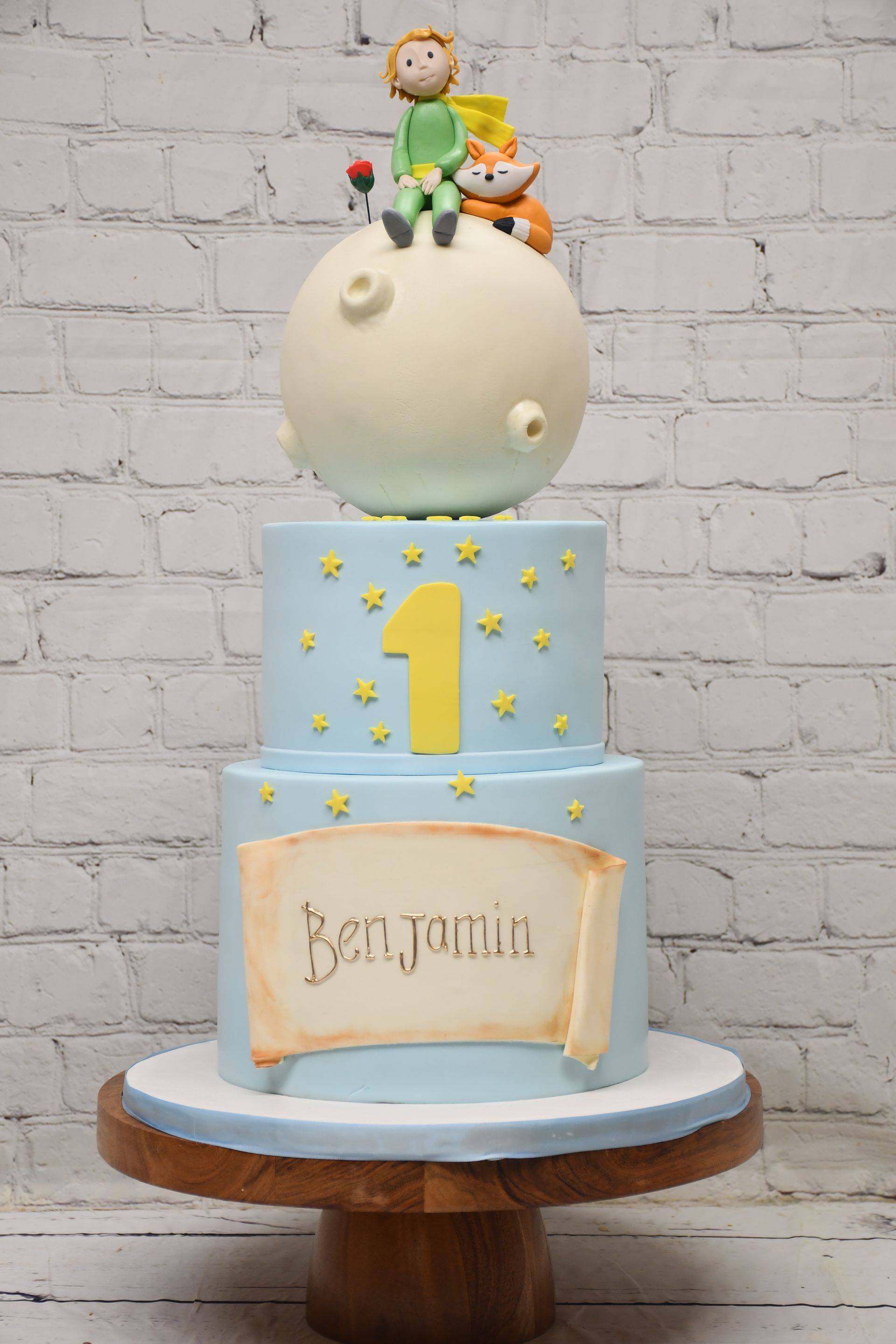 A blue and white cake with a prince on top of it is on a wooden cake stand.