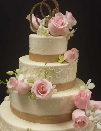 A three tiered wedding cake with pink roses on top