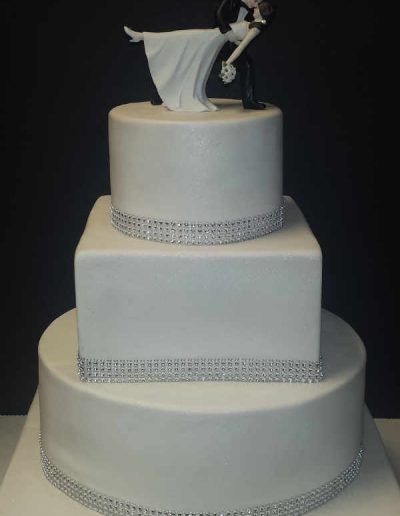 A white wedding cake with a bride and groom figurine on top
