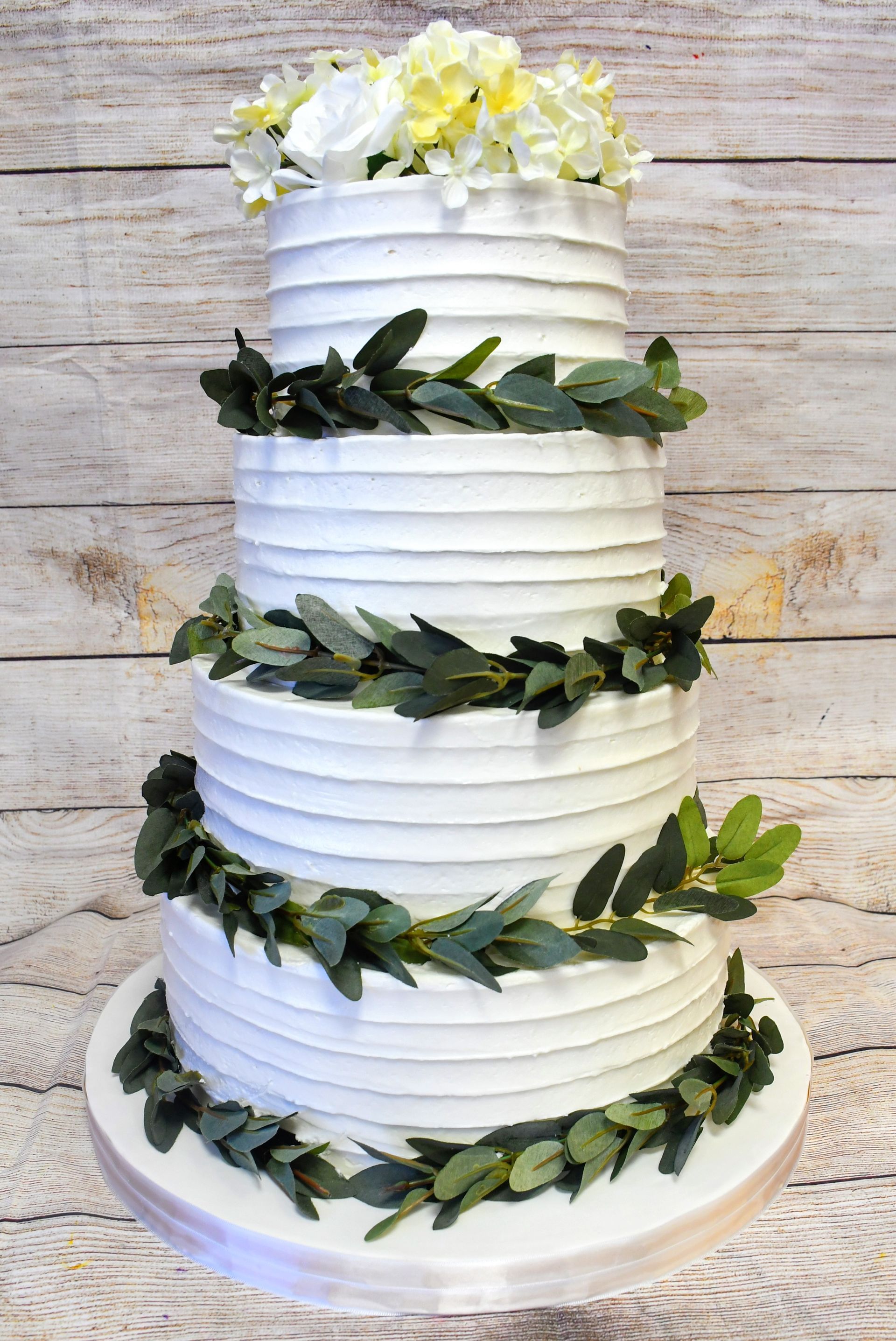 A white wedding cake with green leaves and flowers on a wooden table.