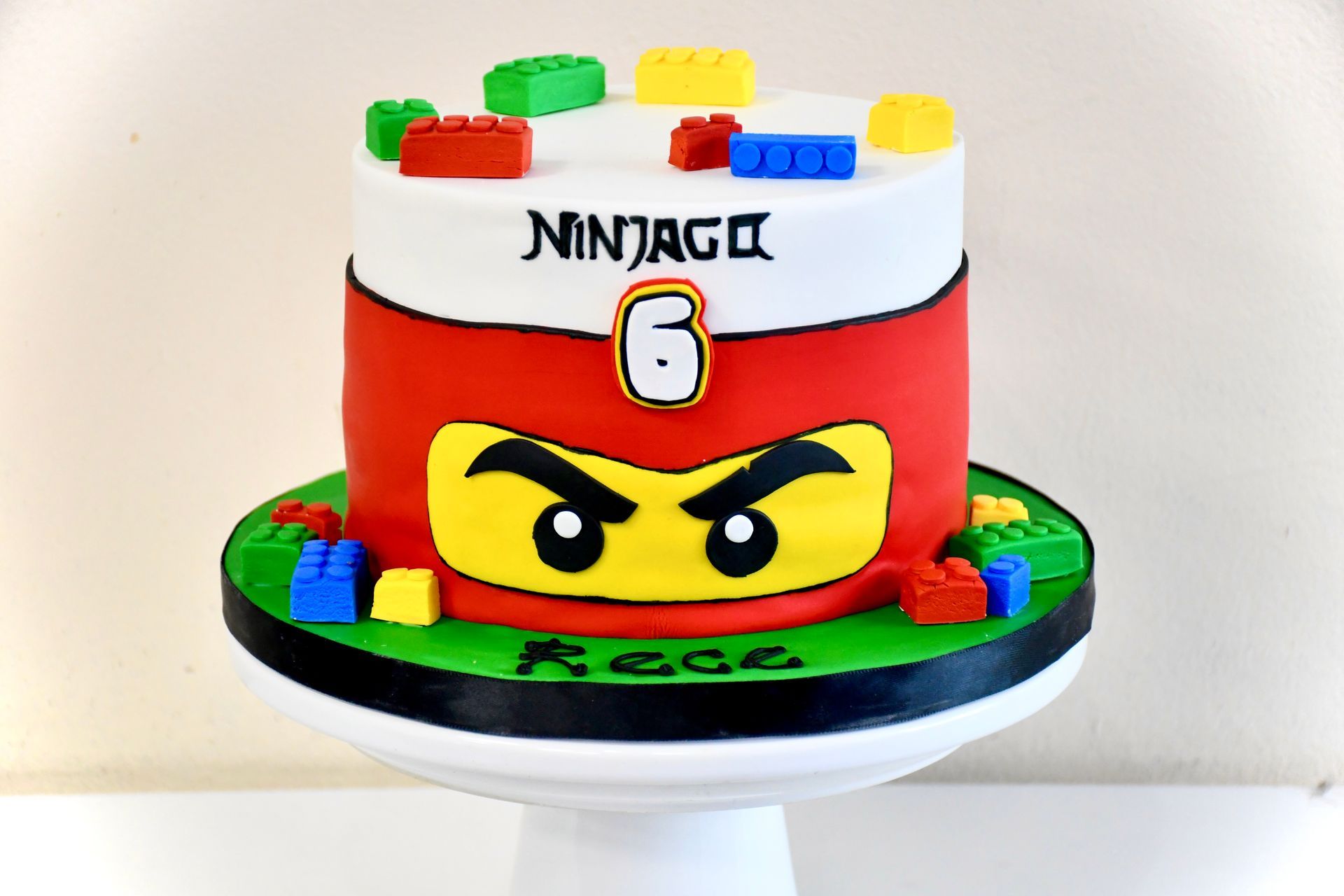 A ninjago cake is sitting on top of a white cake stand.