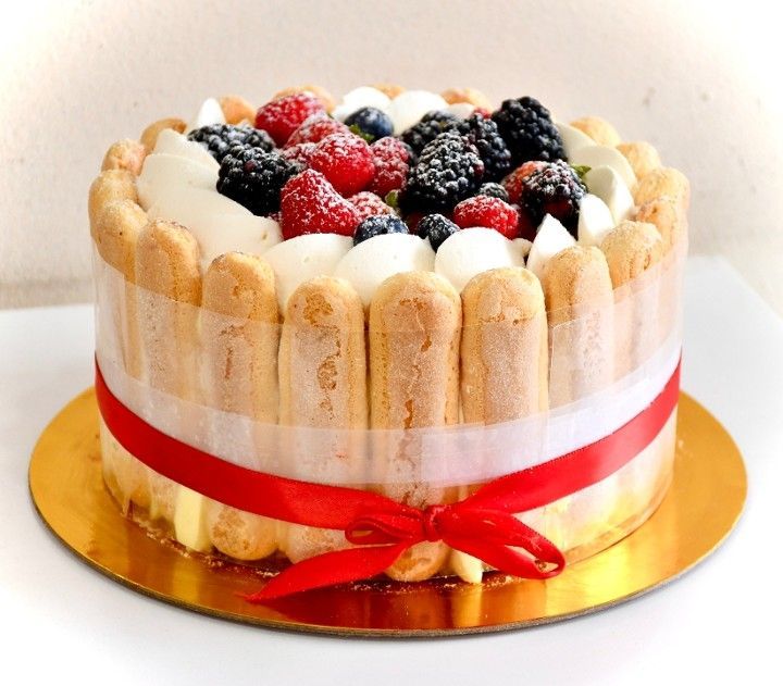 A cake with berries on top and a red ribbon around it