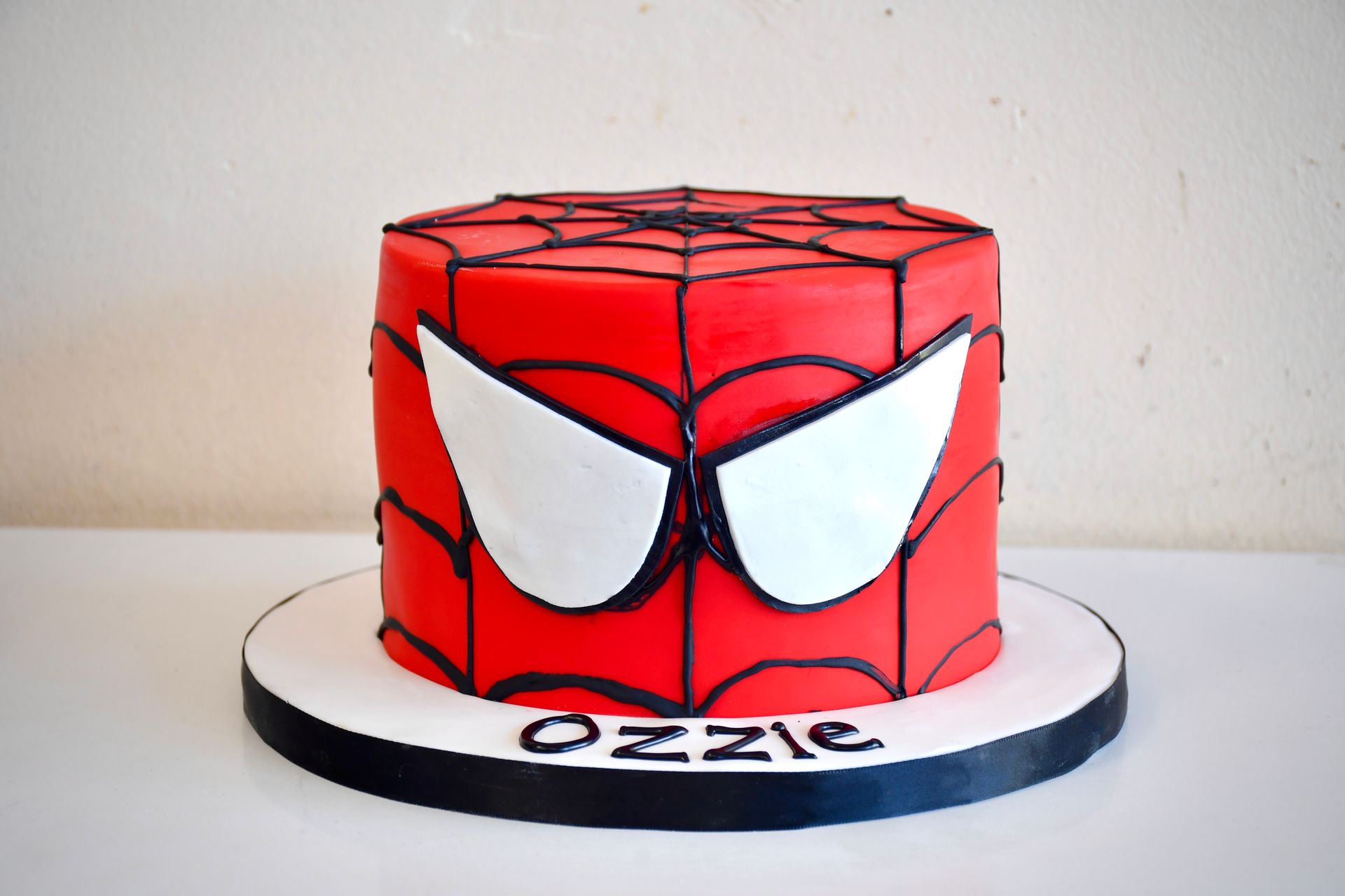 A spiderman cake with the name ozzie on it