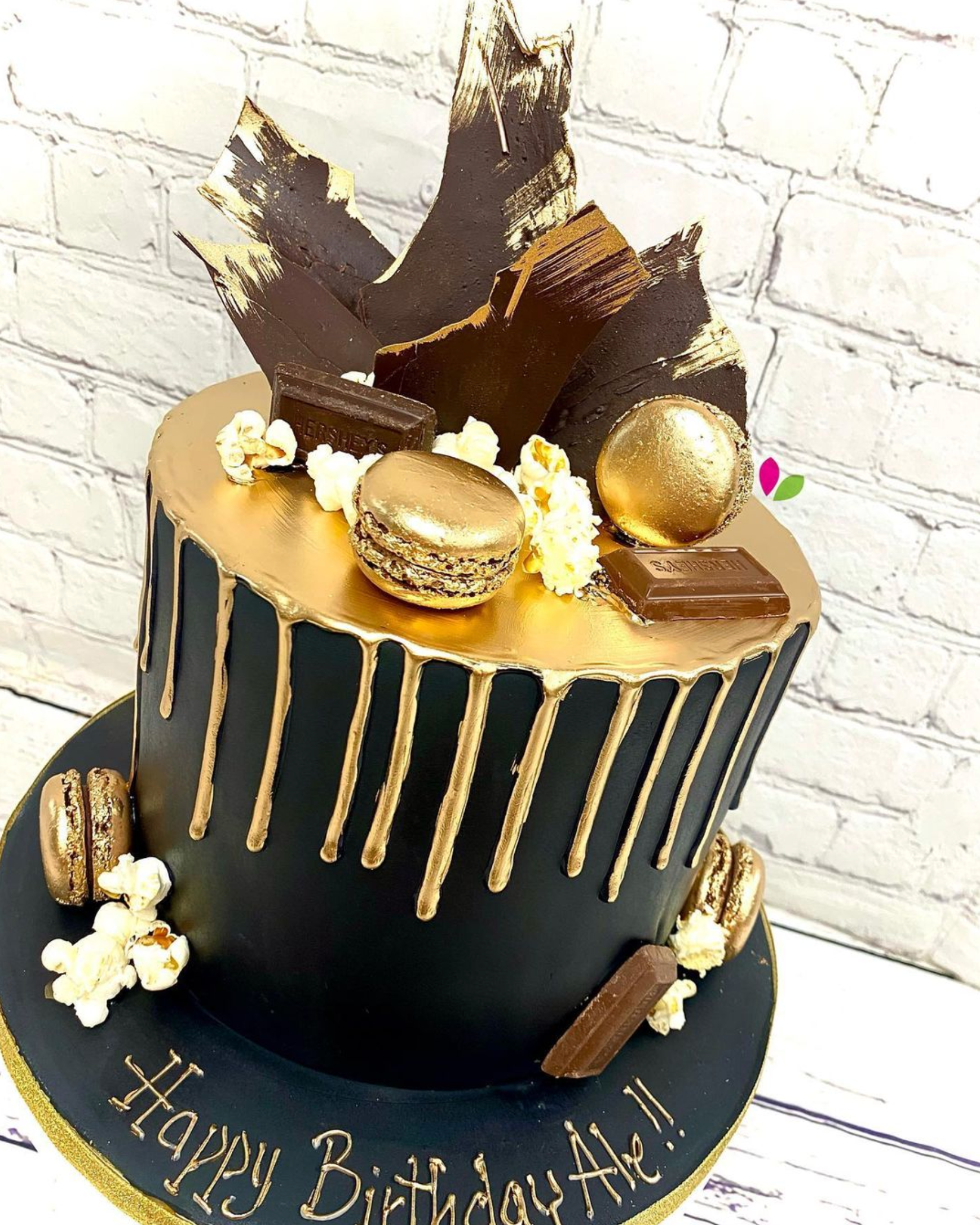 A black and gold birthday cake with a brick wall in the background