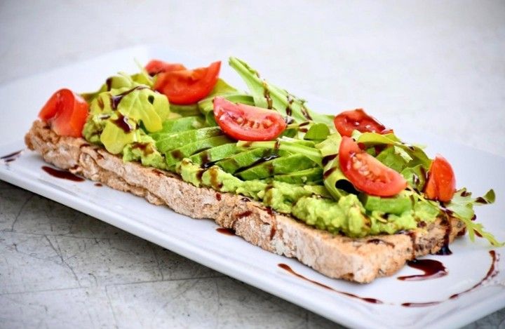 A white plate topped with avocado toast and tomatoes.