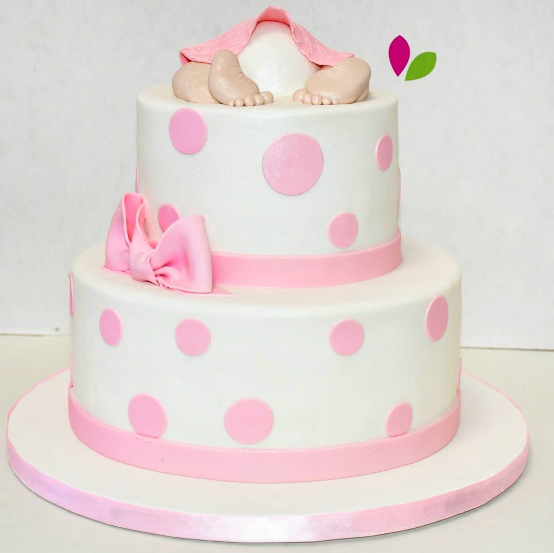 A white cake with pink polka dots and a baby on top