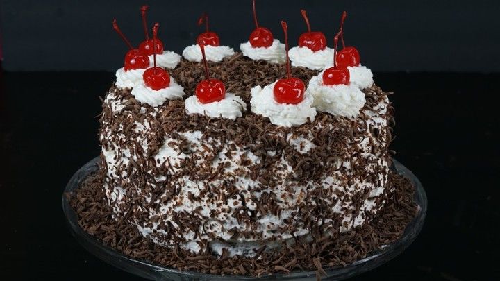 A black forest cake with cherries on top of it on a glass plate.