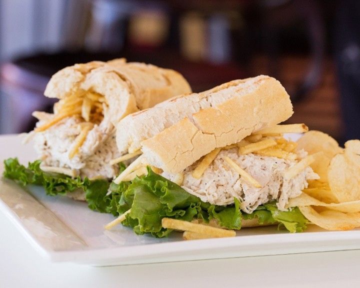 A white plate topped with chicken salad sandwiches and potato chips.