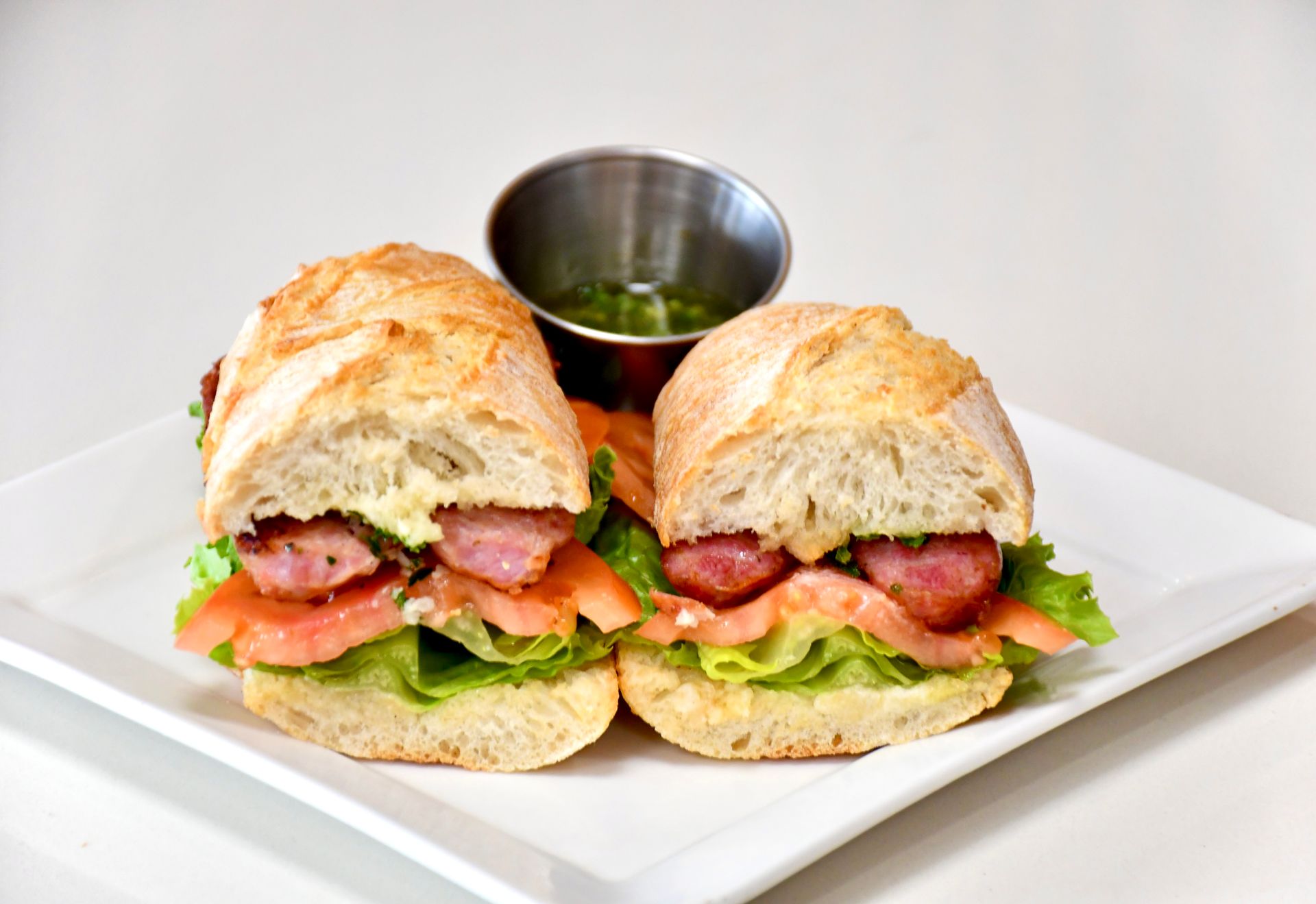 A sandwich is cut in half on a white plate next to a cup of dipping sauce.