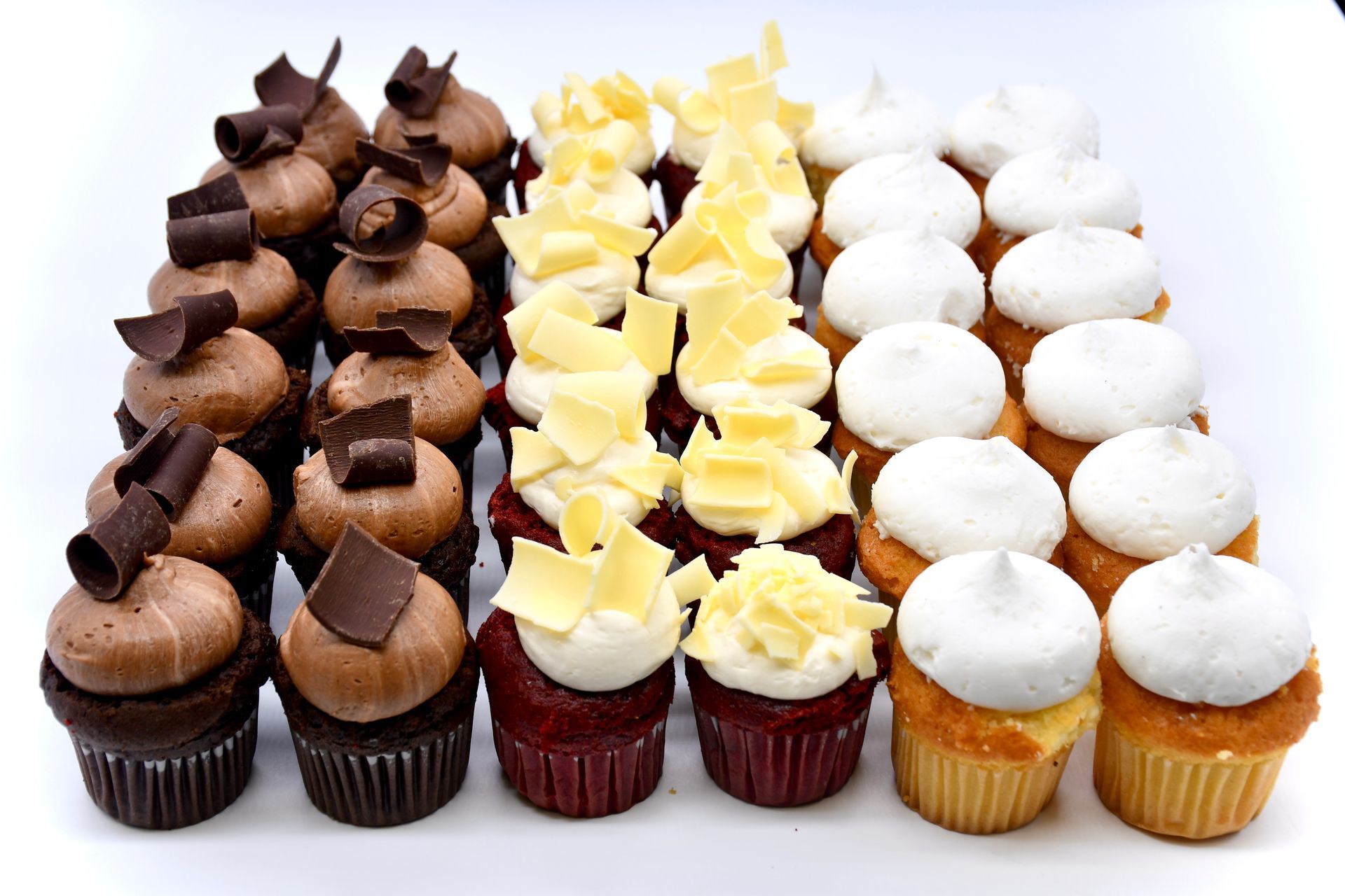 A variety of cupcakes are lined up in a row on a white surface.