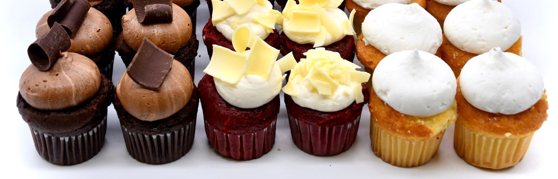 A variety of cupcakes are lined up in a row on a white surface.