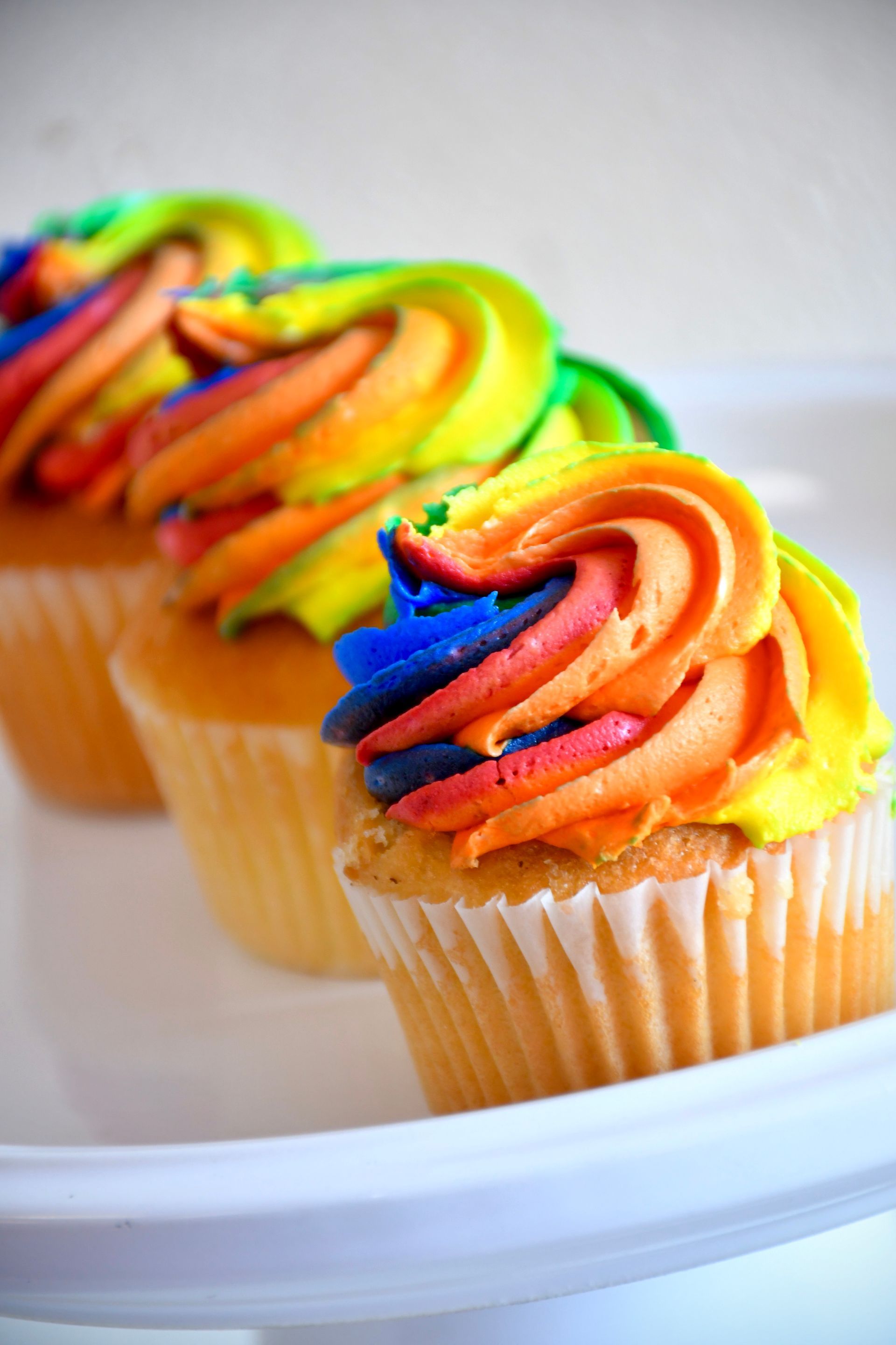 A row of cupcakes with rainbow frosting on a white plate.