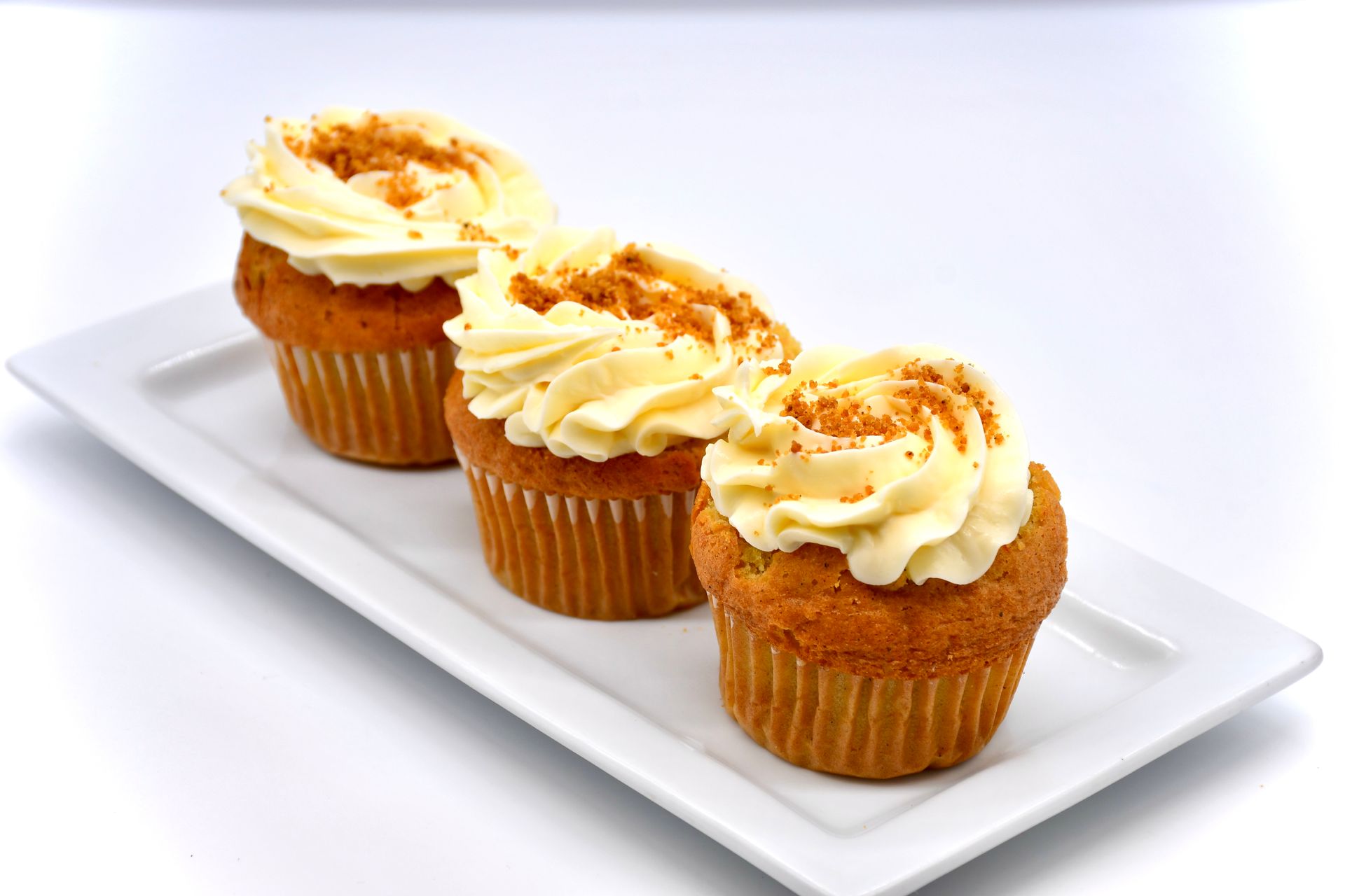 Three carrot cake cupcakes with frosting on a white plate.
