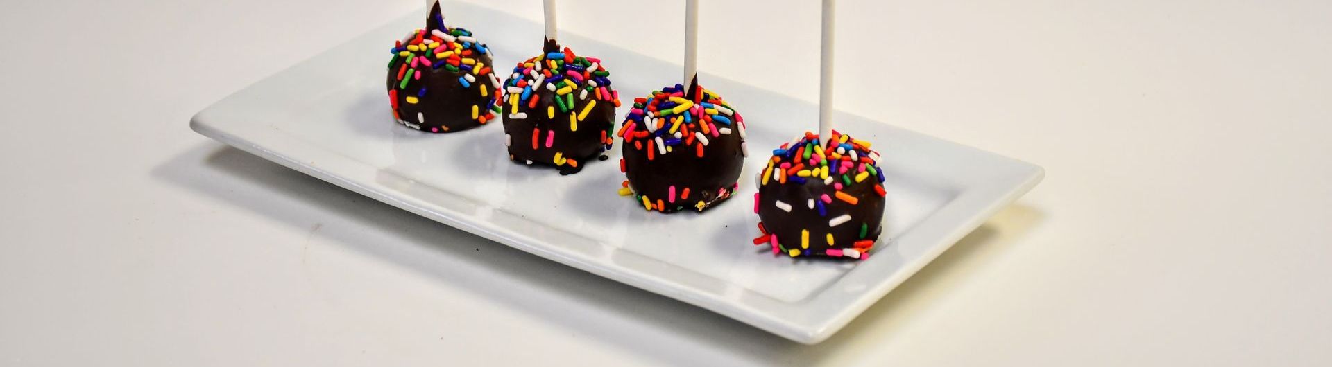 A white plate topped with four cake pops covered in chocolate and sprinkles.