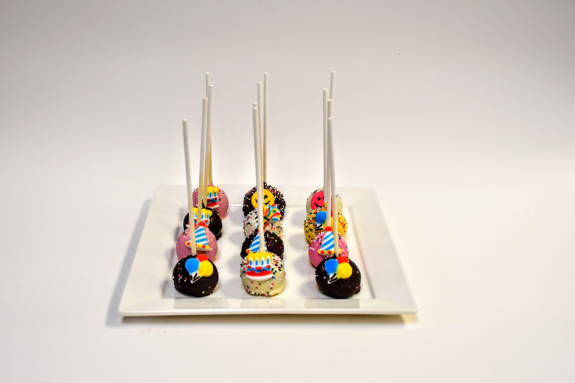 A white plate topped with colorful cake pops on sticks.