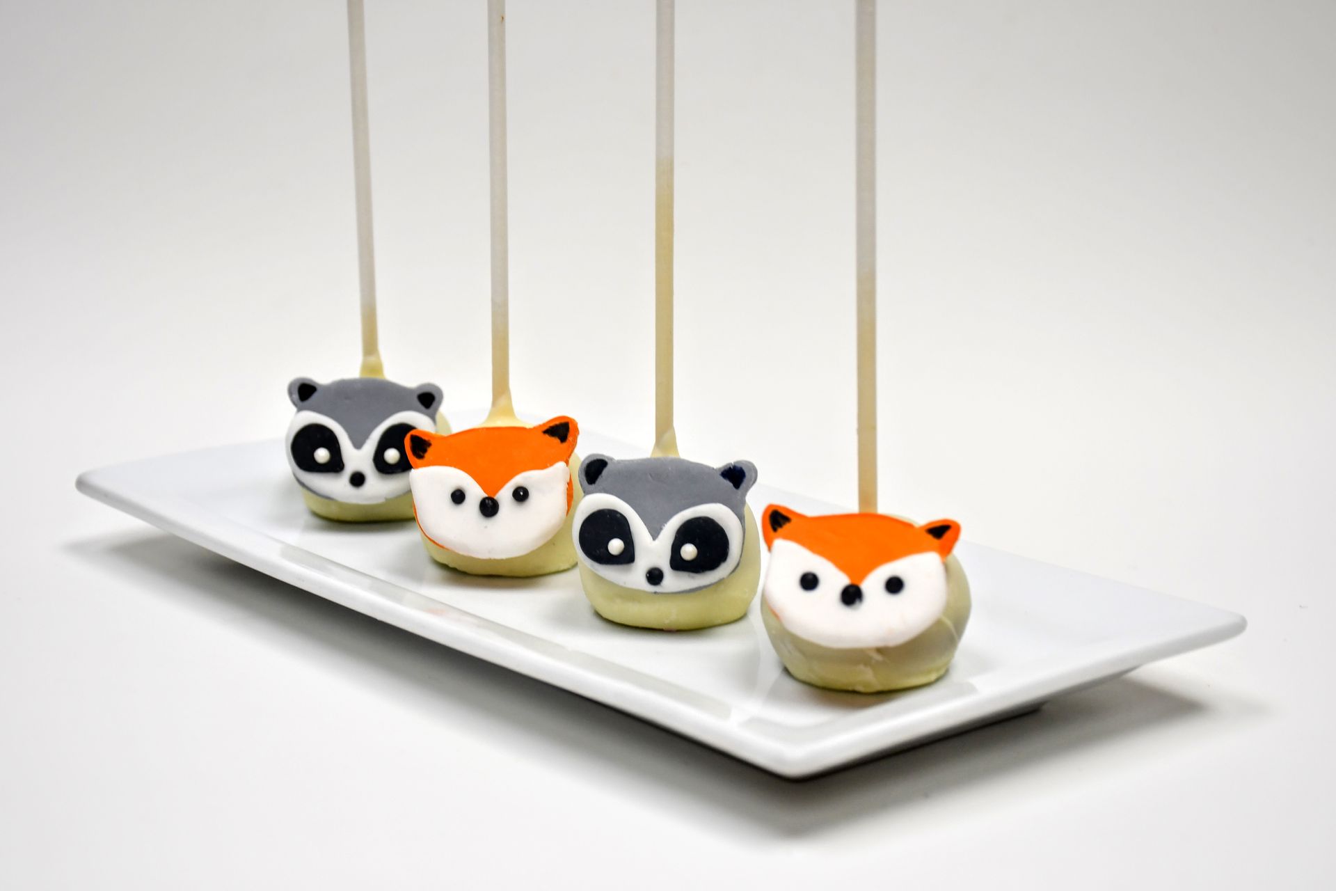 Four cake pops with fox faces on them are on a white plate.