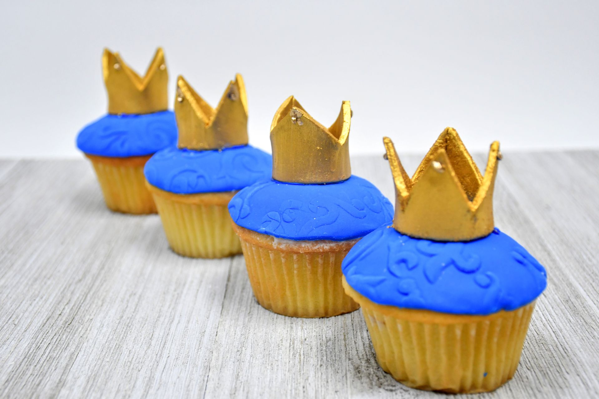 A row of cupcakes with blue frosting and gold crowns on top.